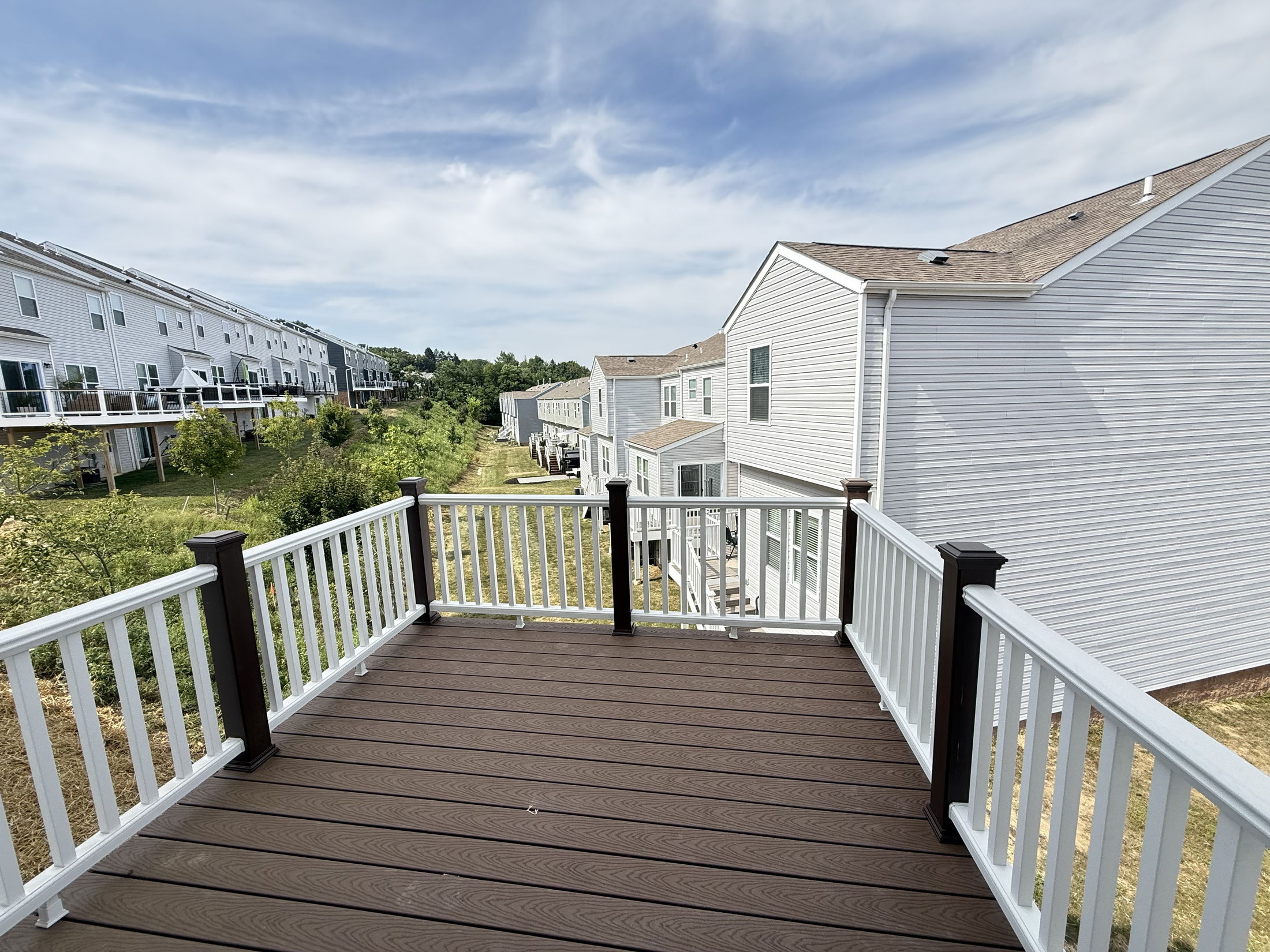 A spacious outdoor deck overlooking suburban townhouses and green space under a partly cloudy sky.
