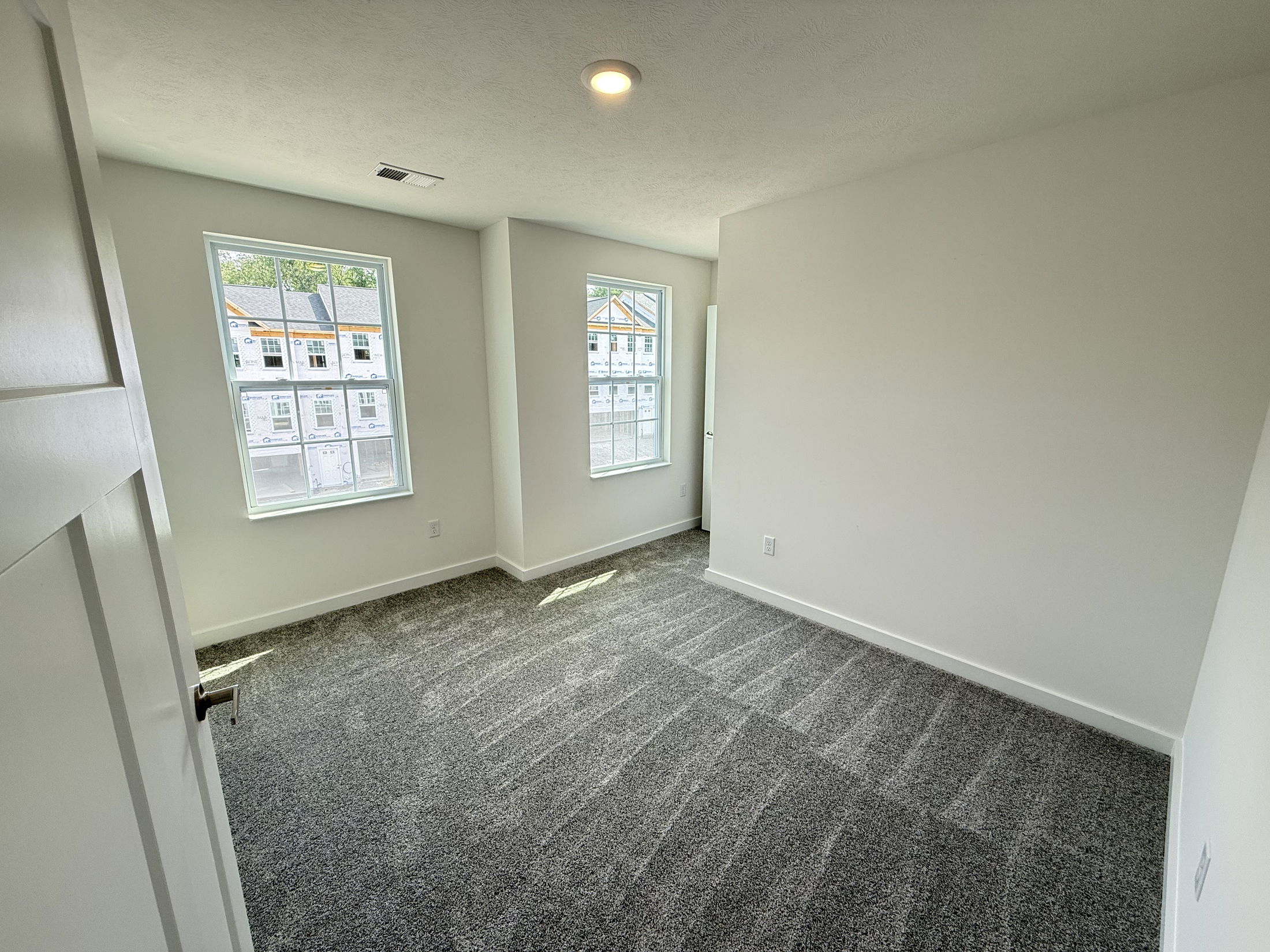 Empty, white-walled room with large windows and fresh gray carpet in a modern home.