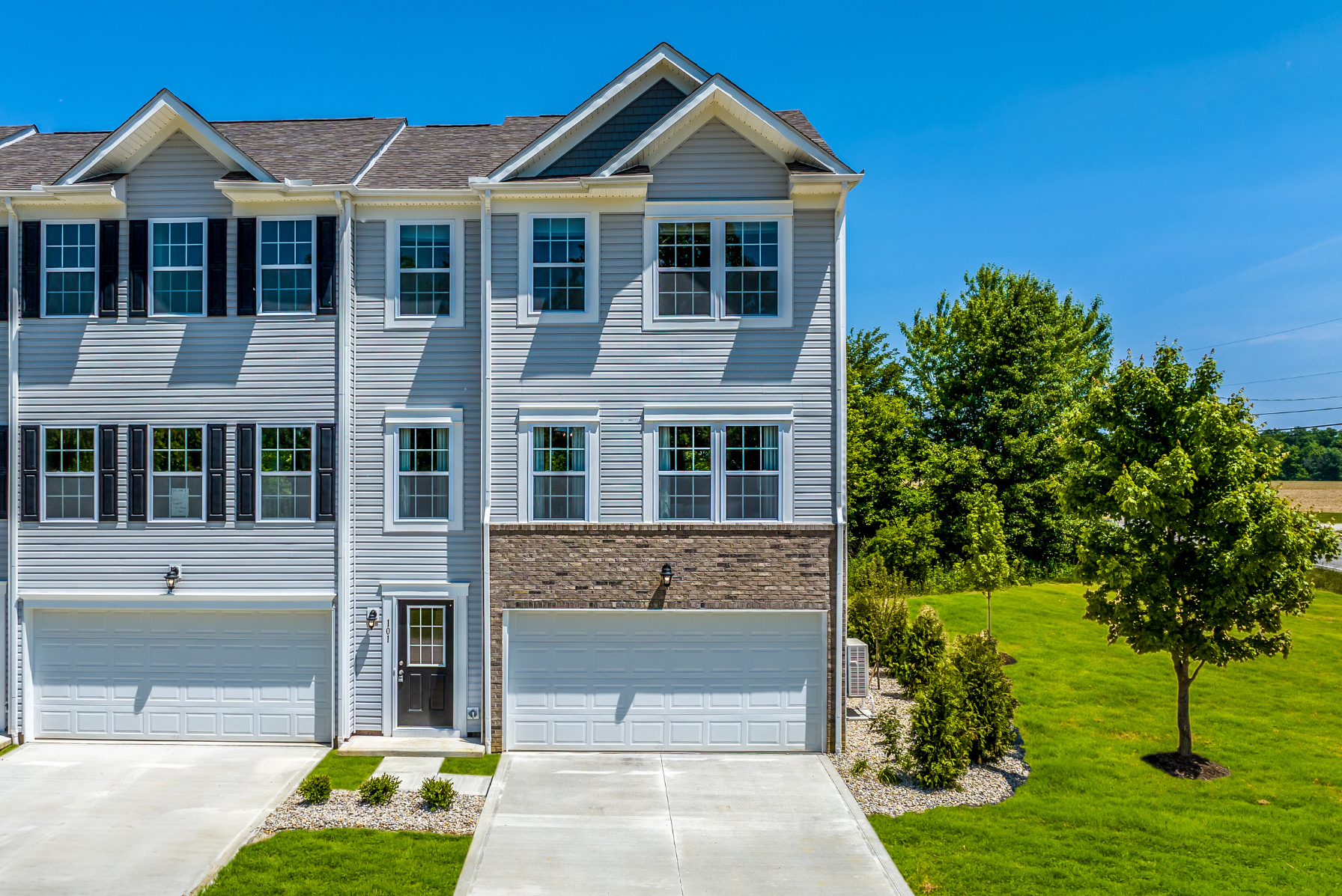 Modern two-story townhouse with double garage and landscaped front yard on a sunny day.