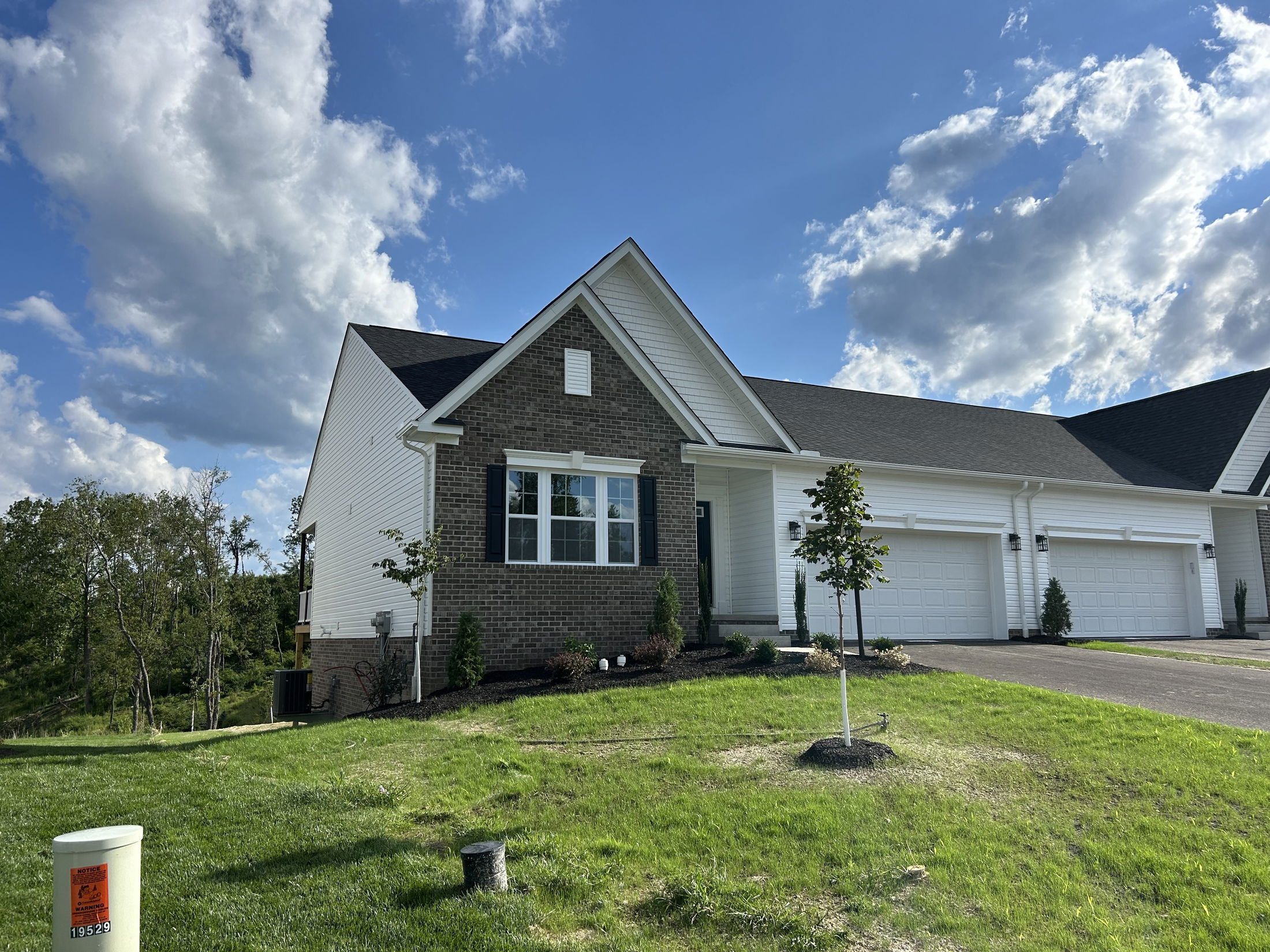 Exterior view of a modern suburban house with a brick facade, white siding, two-car garage, and a well-maintained lawn under a blue sky with clouds.