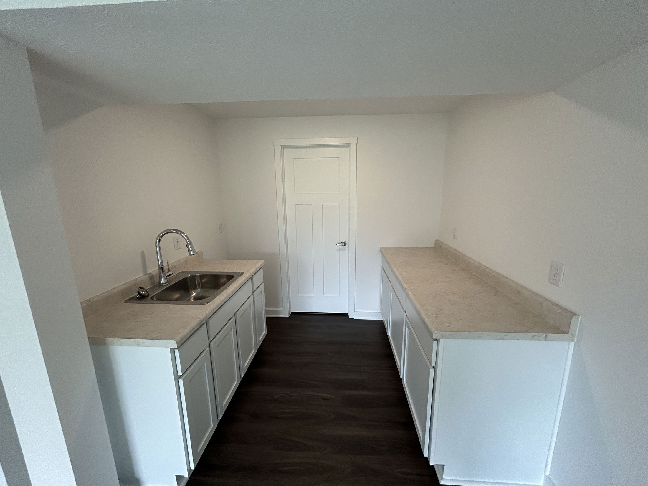 Modern small kitchen with white cabinets, dark flooring, and stainless steel sink.
