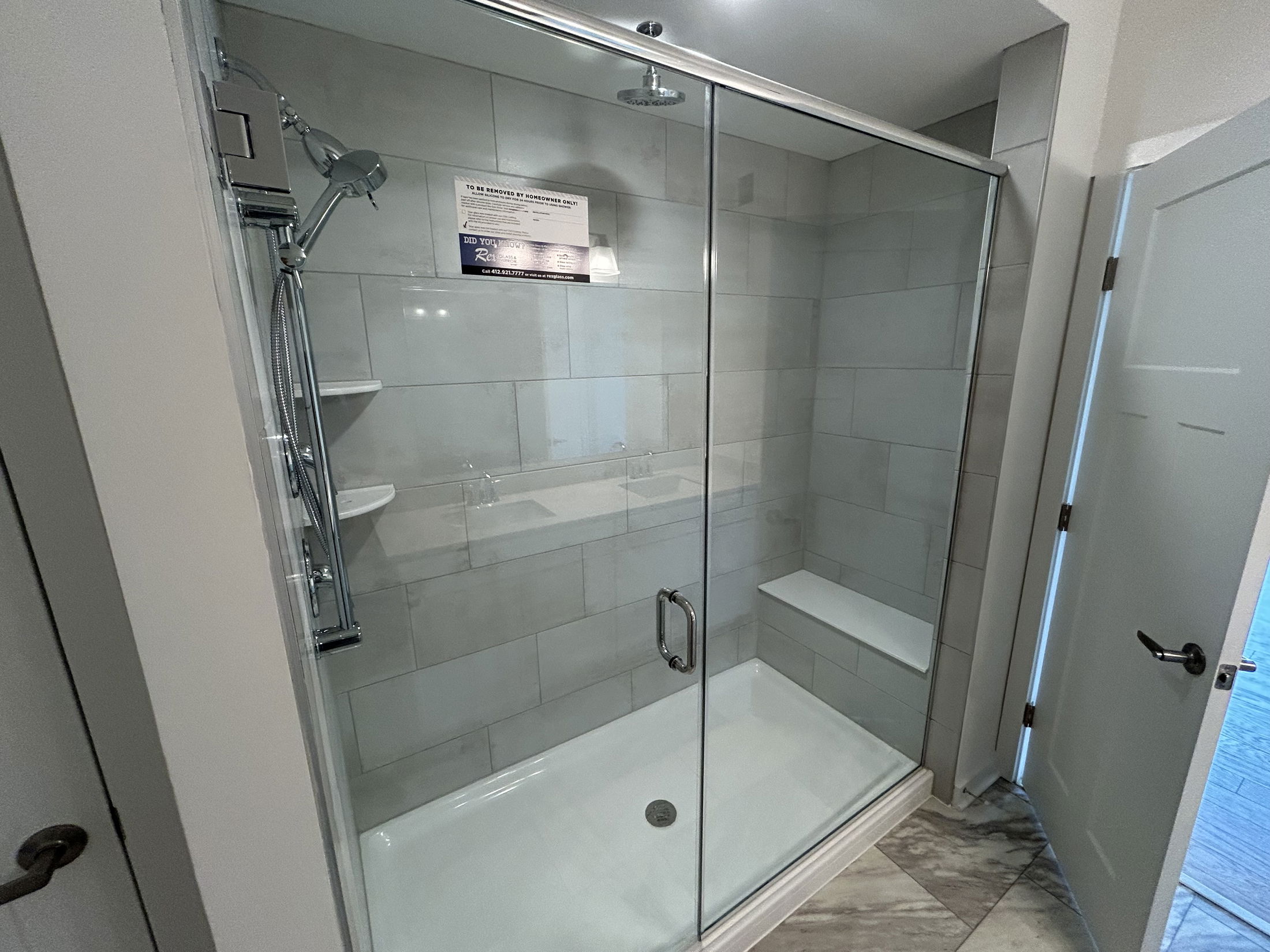 Modern bathroom with a glass-enclosed shower featuring a rainfall showerhead and built-in bench against tiled walls.