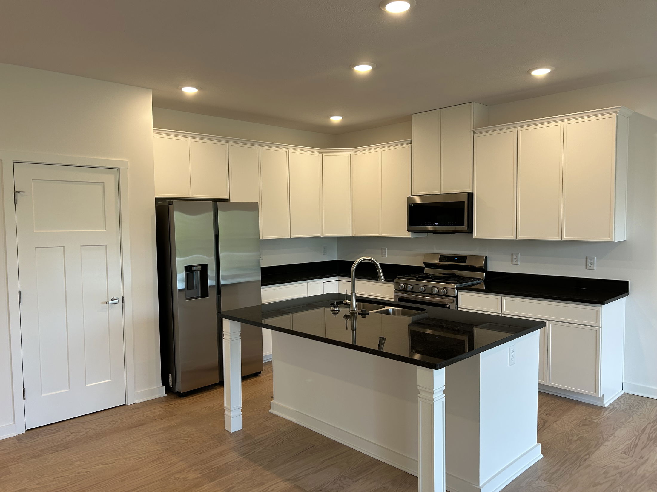 Modern kitchen with white cabinets, black countertops, stainless steel appliances, and a central island with a built-in sink.