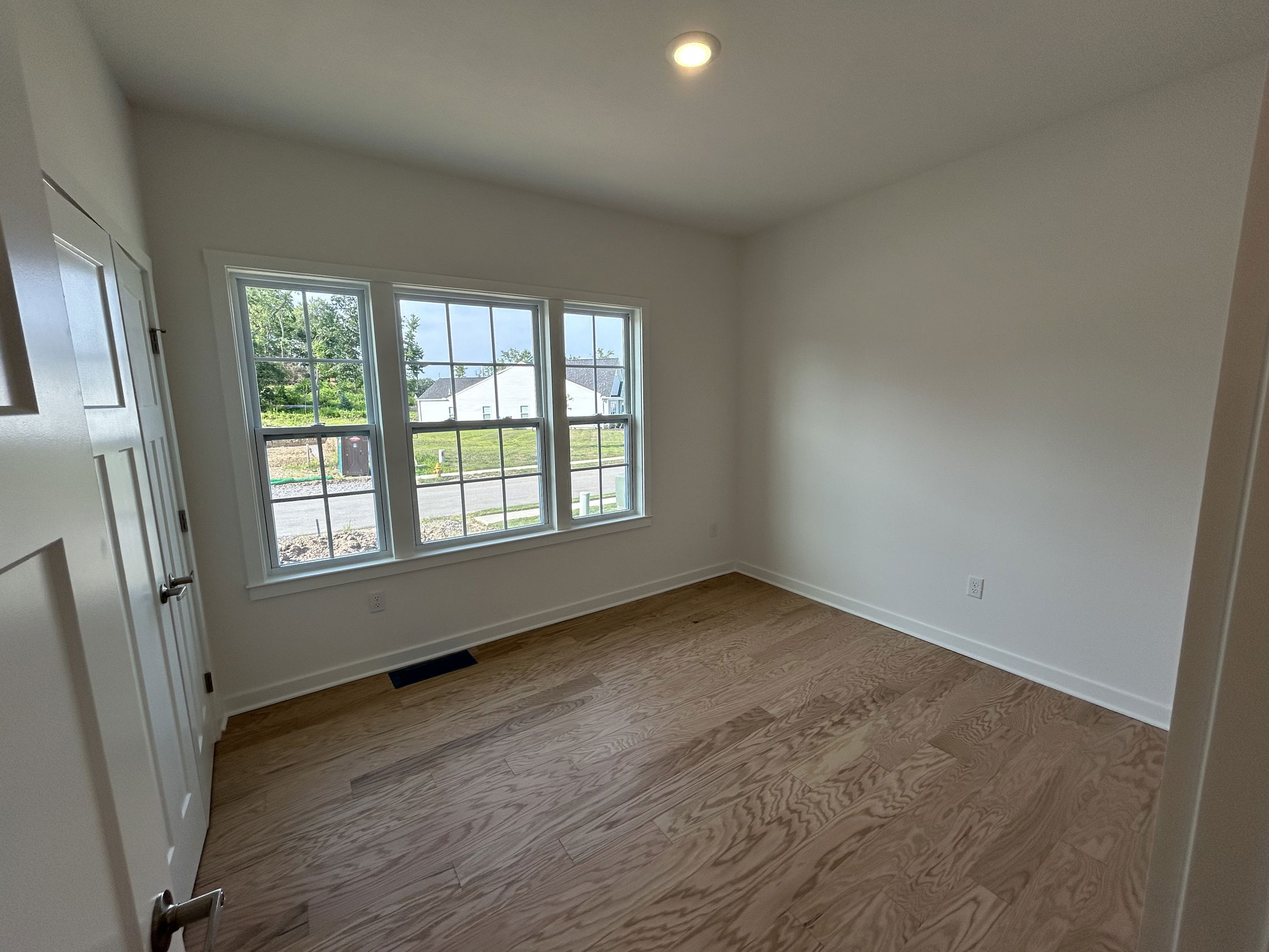 Bright and airy empty room with large windows, white walls, and wooden flooring.