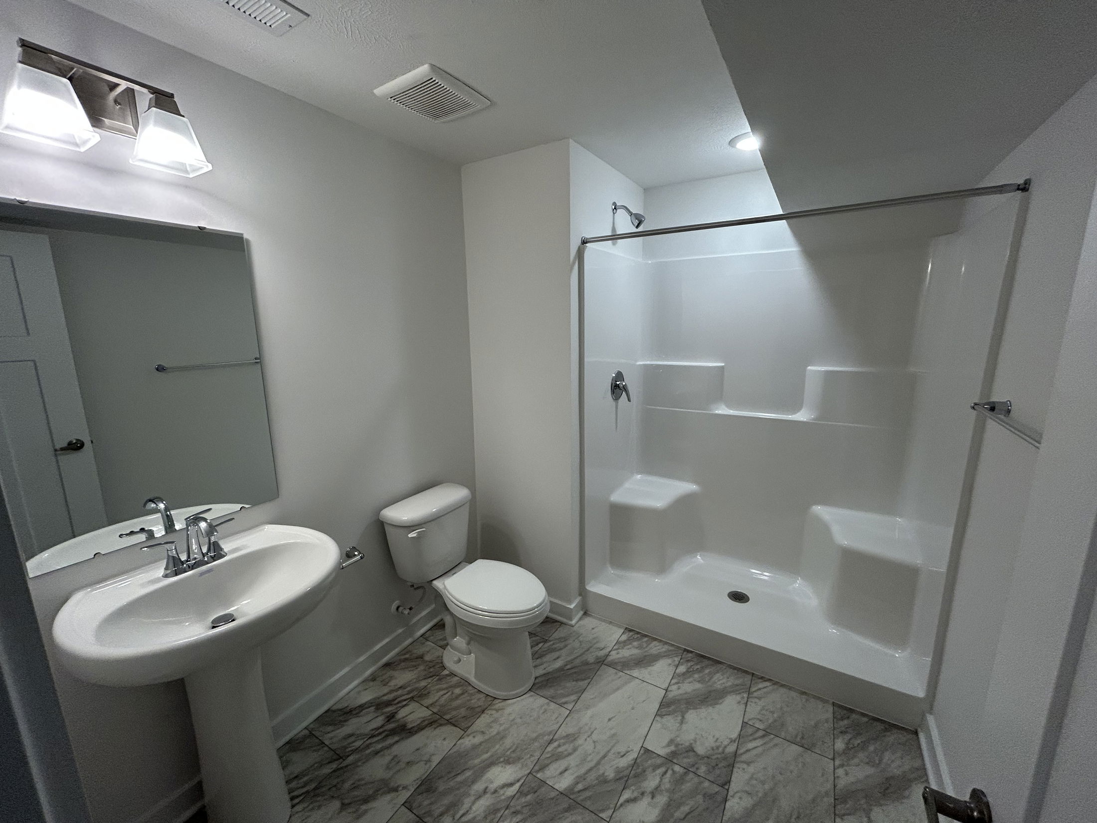 Modern bathroom with white pedestal sink, toilet, and a spacious walk-in shower featuring built-in seating and tiled flooring.