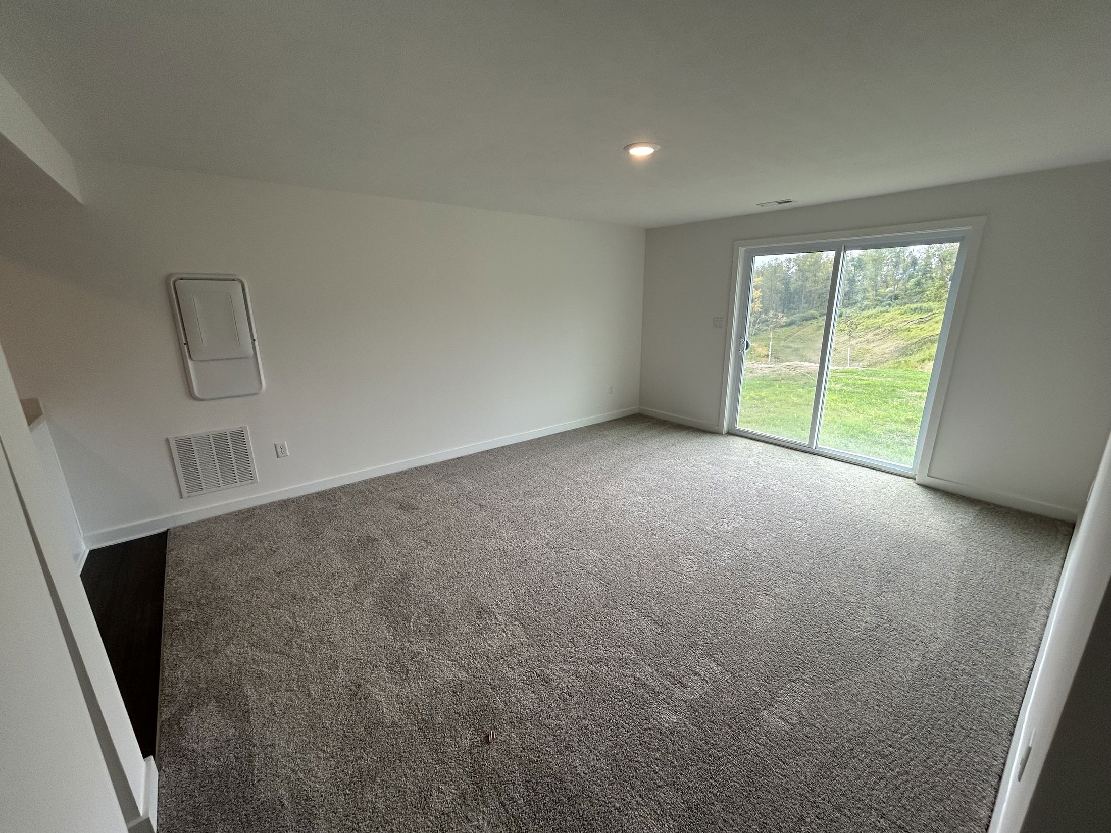Spacious, carpeted living room with a large sliding glass door opening to a green backyard.