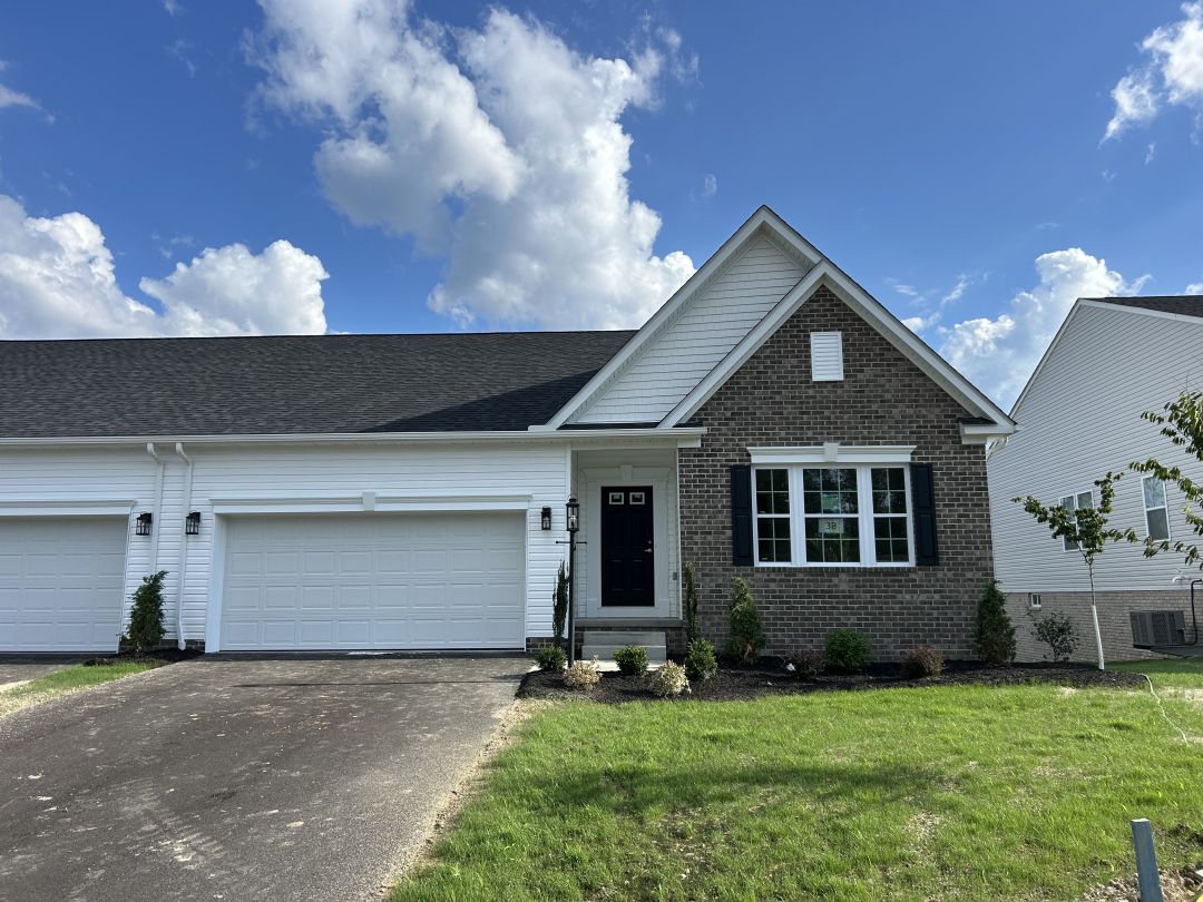 Modern single-story brick home with a two-car garage, set against a blue sky with scattered clouds.