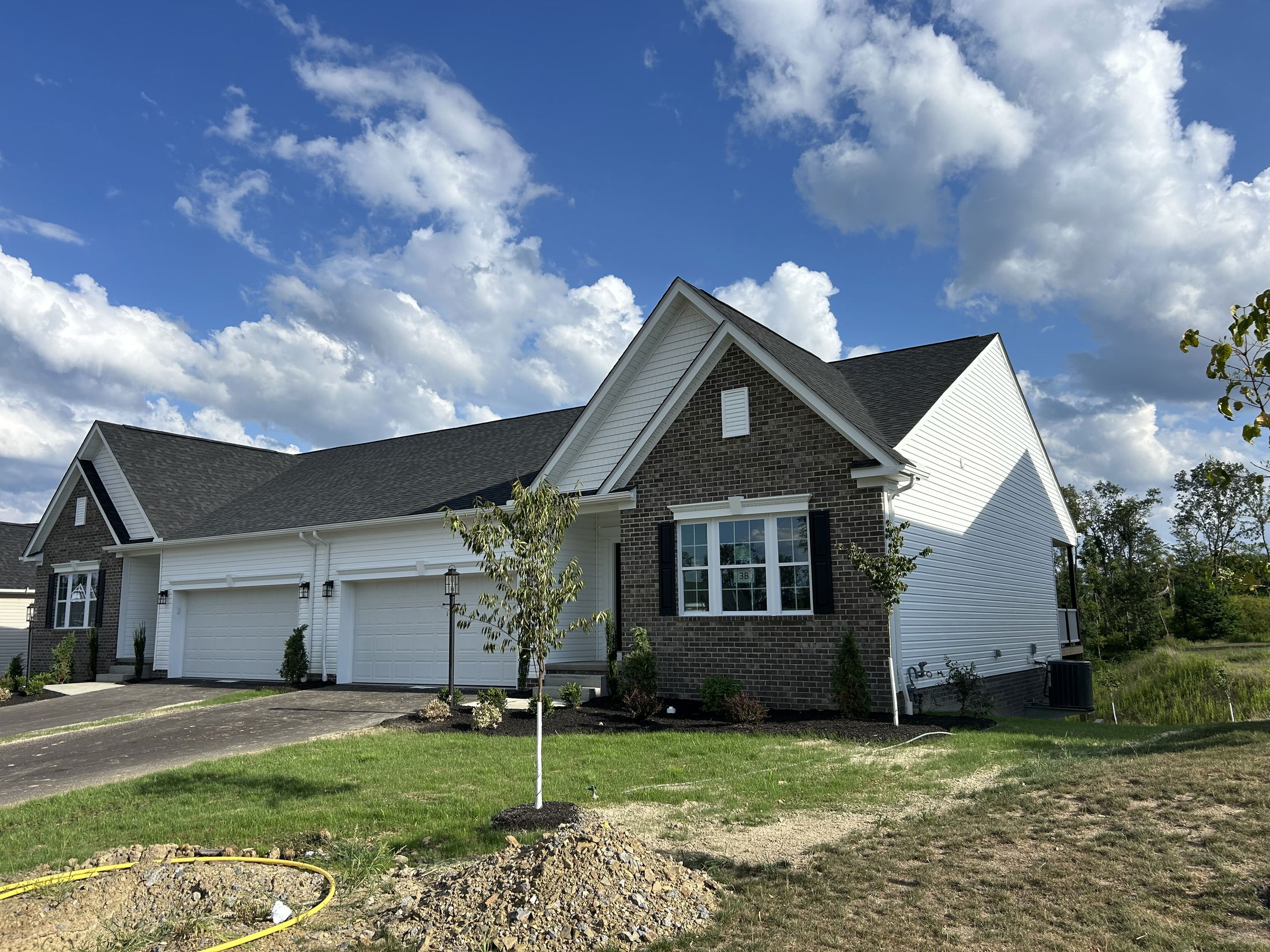 Newly built suburban house with a brick facade, landscaped front yard, and clear blue sky.