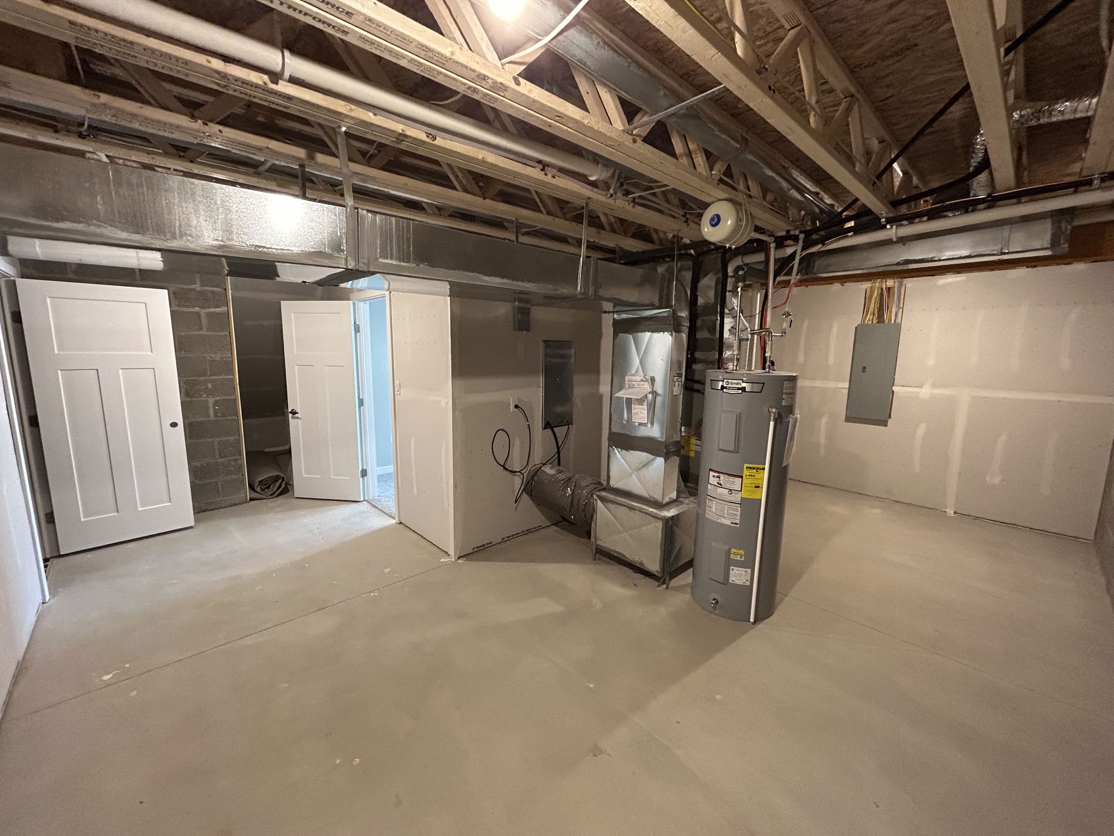 Spacious basement with exposed ceiling beams, HVAC unit, water heater, and utility doors.