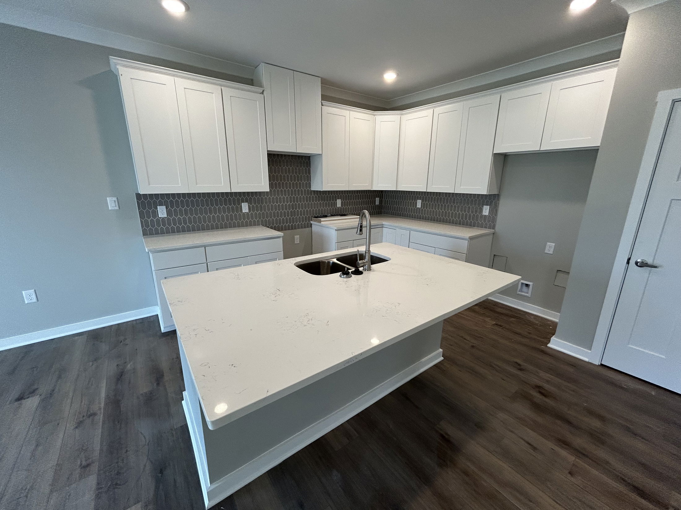 Modern kitchen with white cabinets, a large island featuring a marble countertop and sink, and a gray hexagonal tile backsplash.