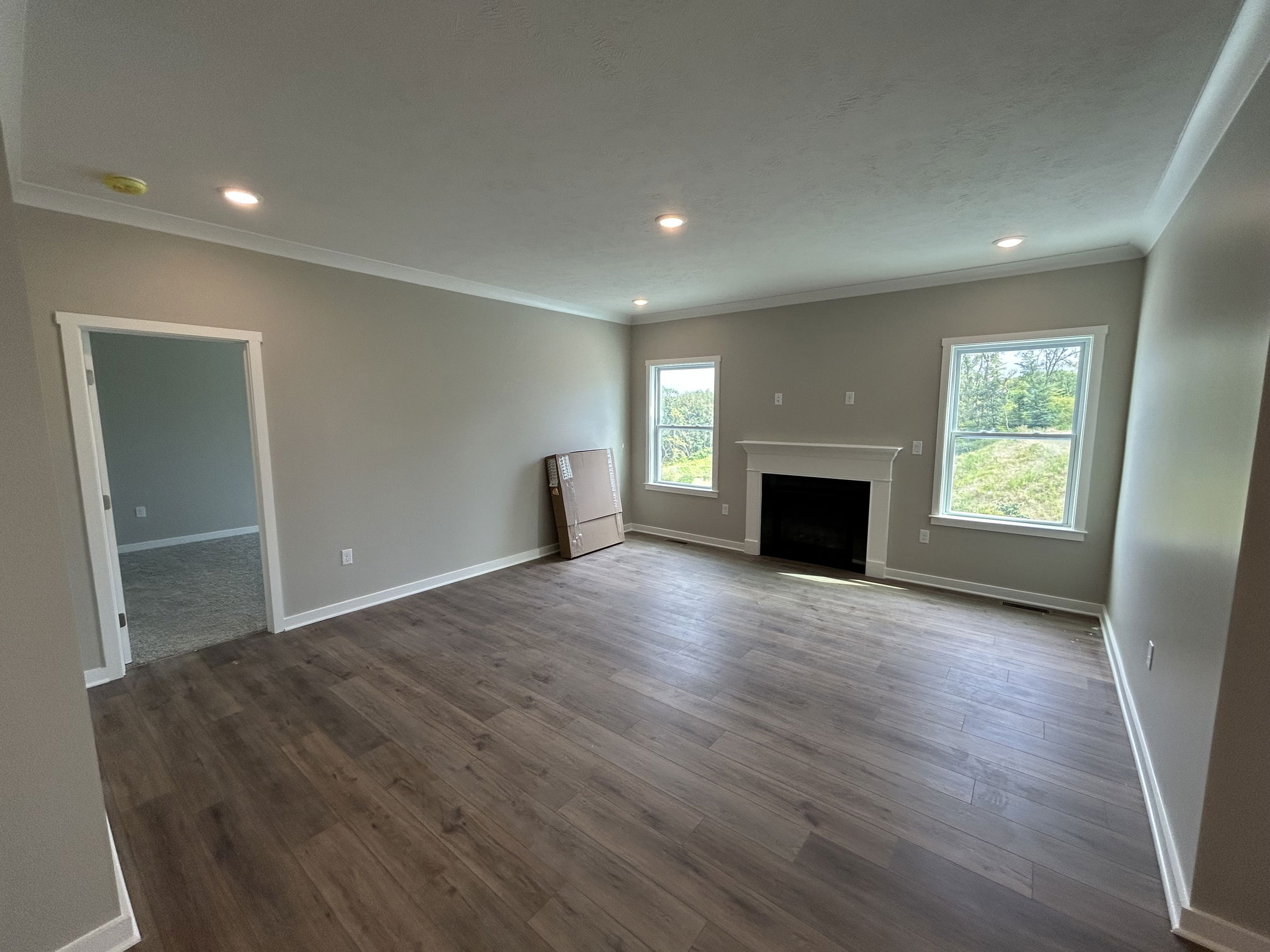 Spacious living room with hardwood floors, two large windows, and a central fireplace, connected to an adjacent carpeted room.