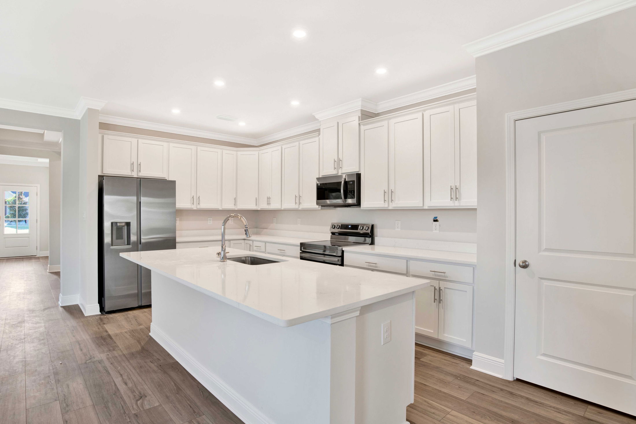 Modern kitchen with white cabinets, stainless steel appliances, and a central island featuring a sleek sink under recessed lighting.