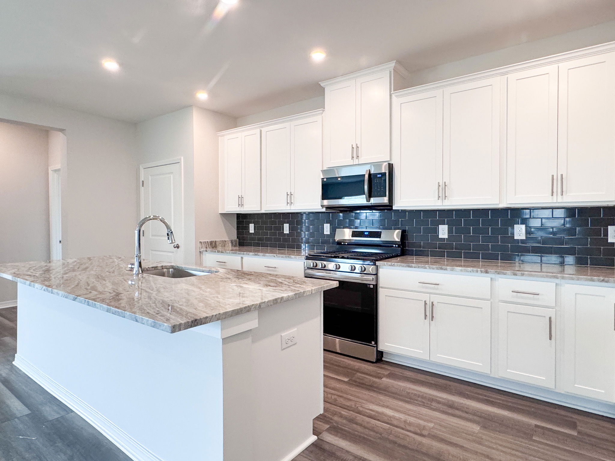 Modern kitchen with white cabinetry, marble countertops, and stainless steel appliances featuring a subway tile backsplash.