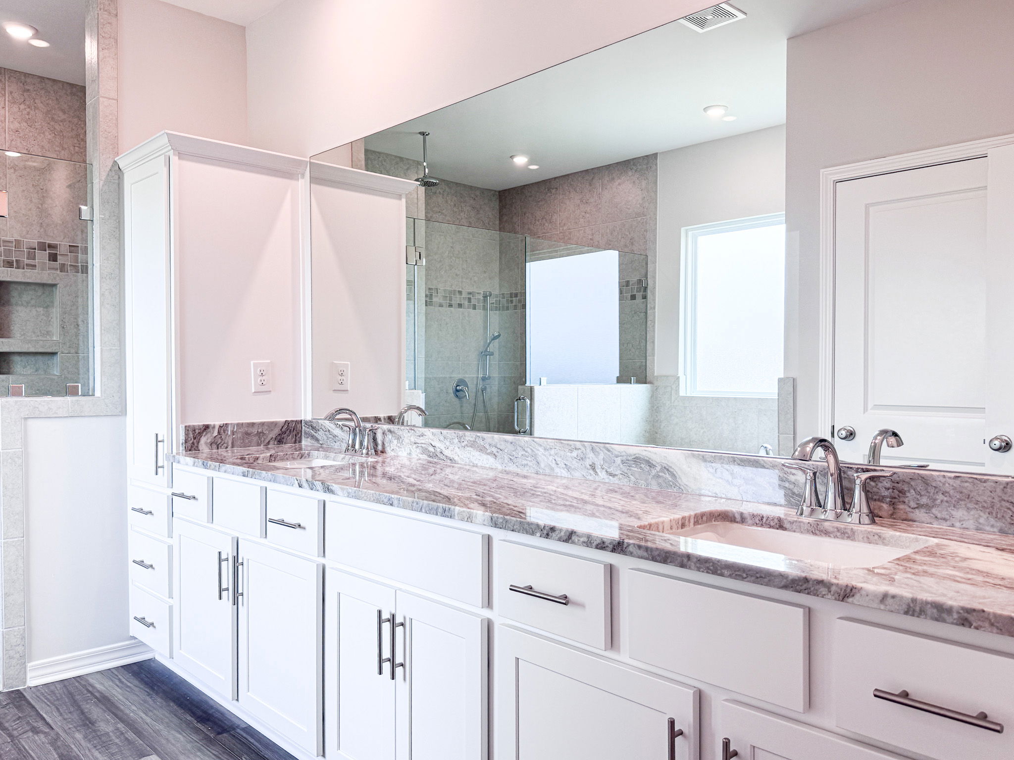 Modern white bathroom with dual sinks, marble countertops, and a large mirror reflecting a spacious shower area.