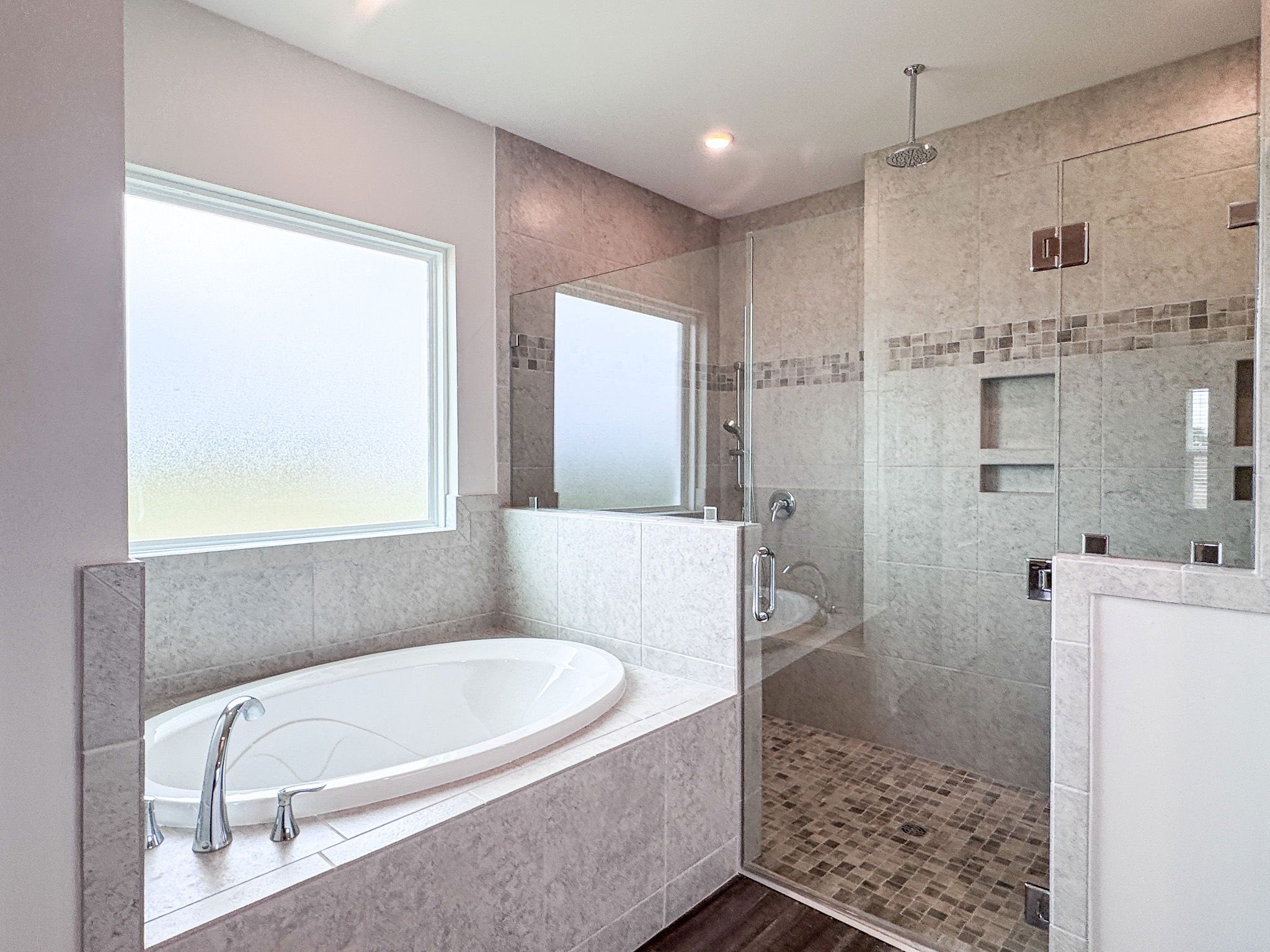 Modern bathroom with a glass-enclosed shower and a freestanding bathtub, featuring gray tiles and natural light from a frosted window.