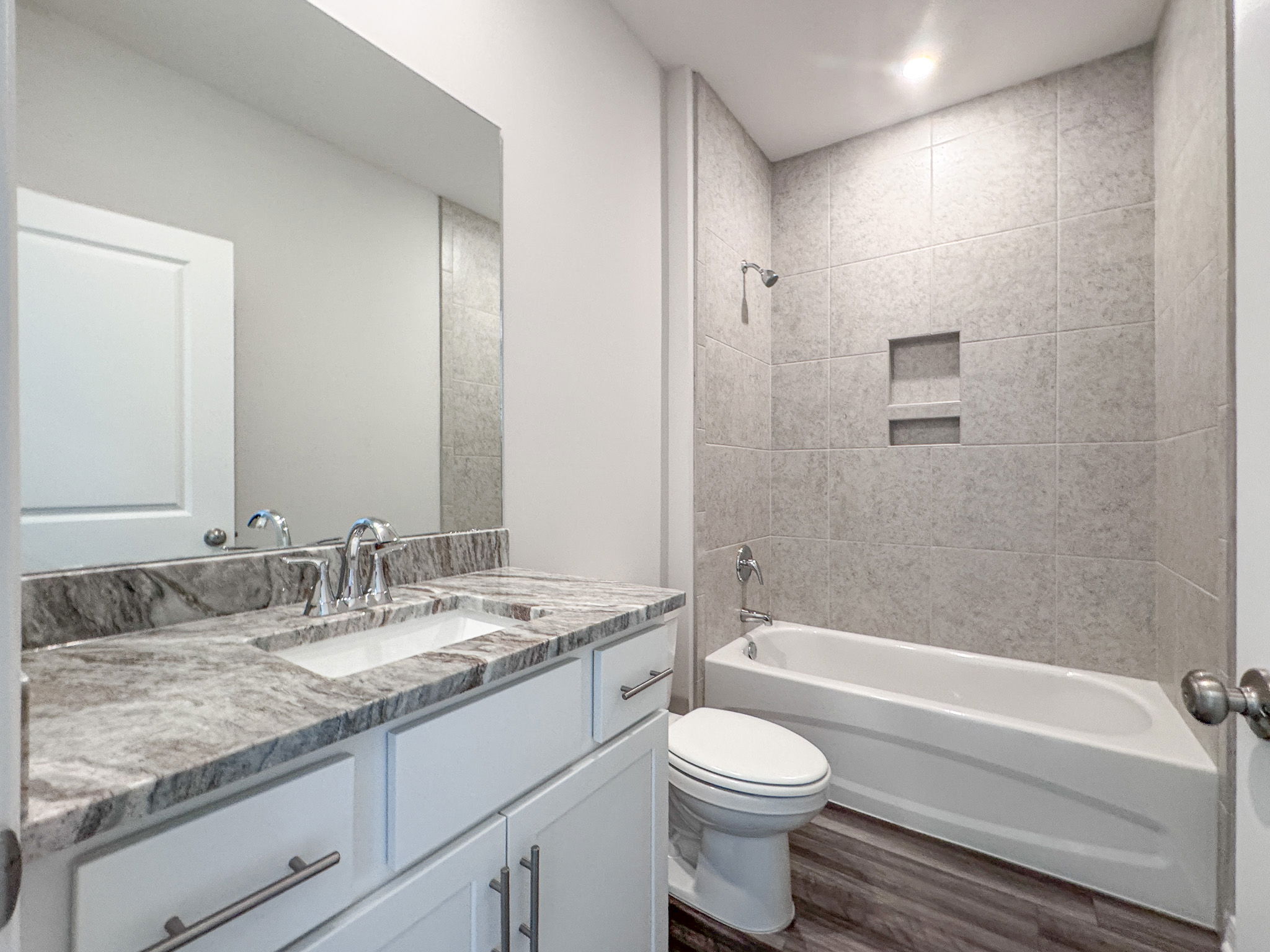 Modern bathroom with a spacious granite countertop, white cabinetry, and a tiled shower and bathtub combination.
