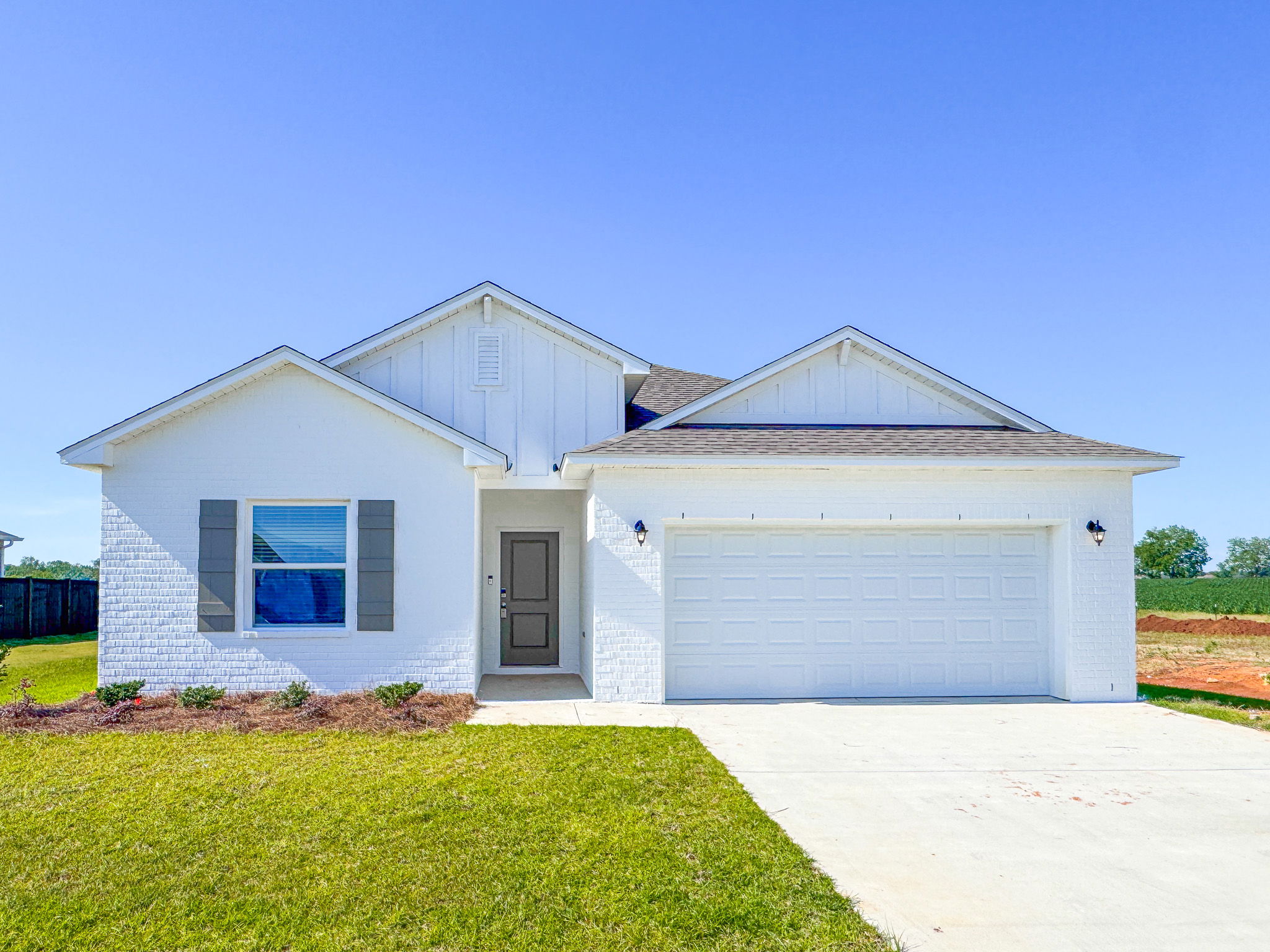 Newly constructed white brick single-story home with a two-car garage and a spacious front yard.