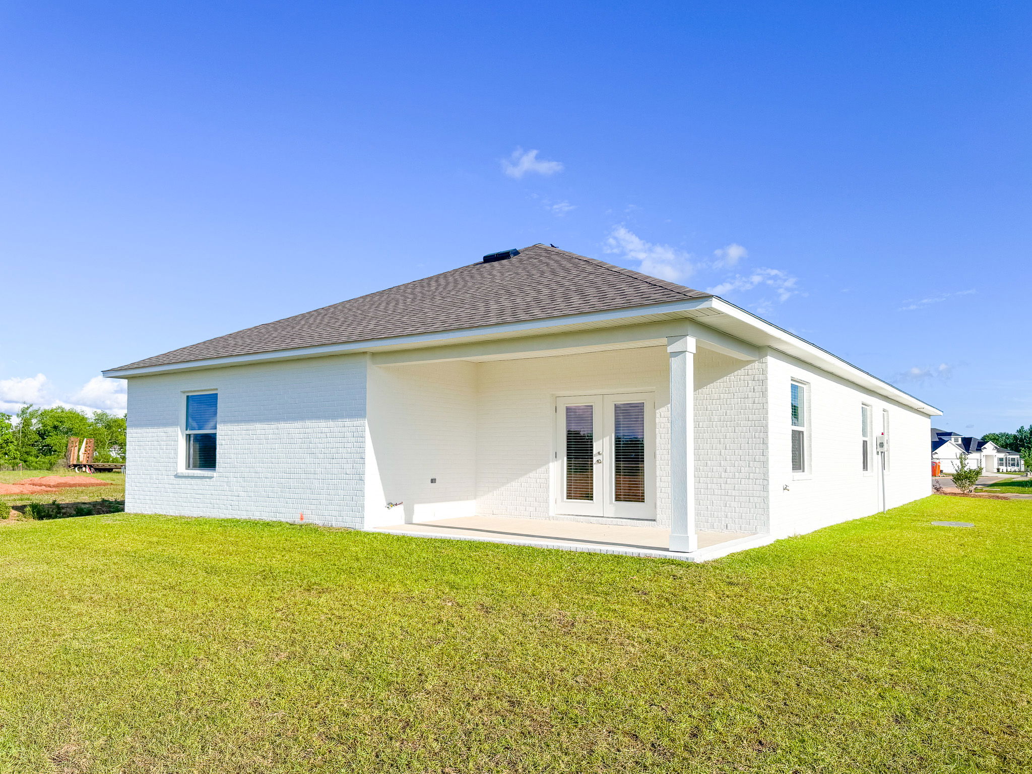 Modern white brick home with a spacious backyard under a clear blue sky.