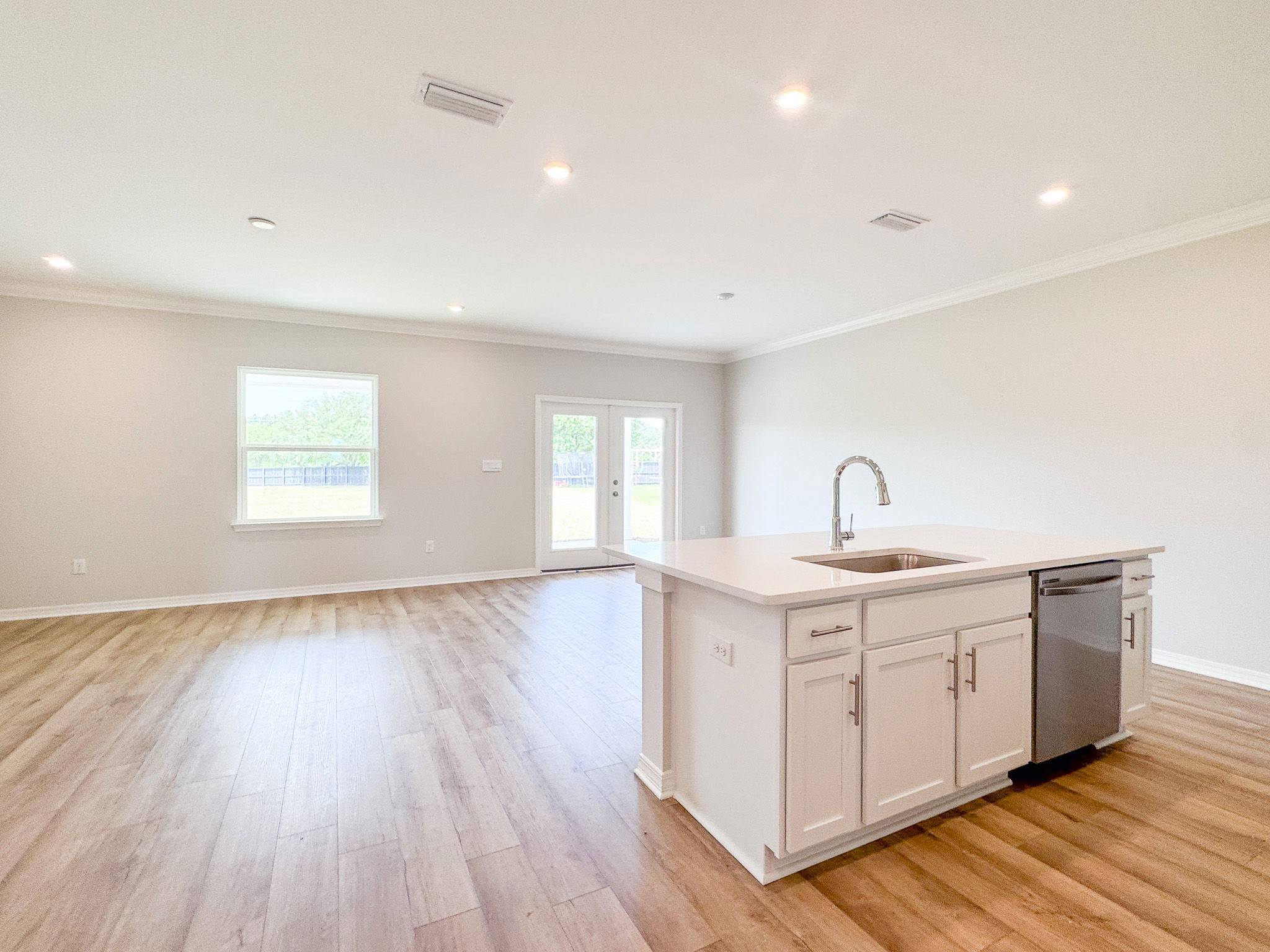 Modern open-concept kitchen with white cabinets, island sink, and hardwood floors in a spacious, well-lit home interior.