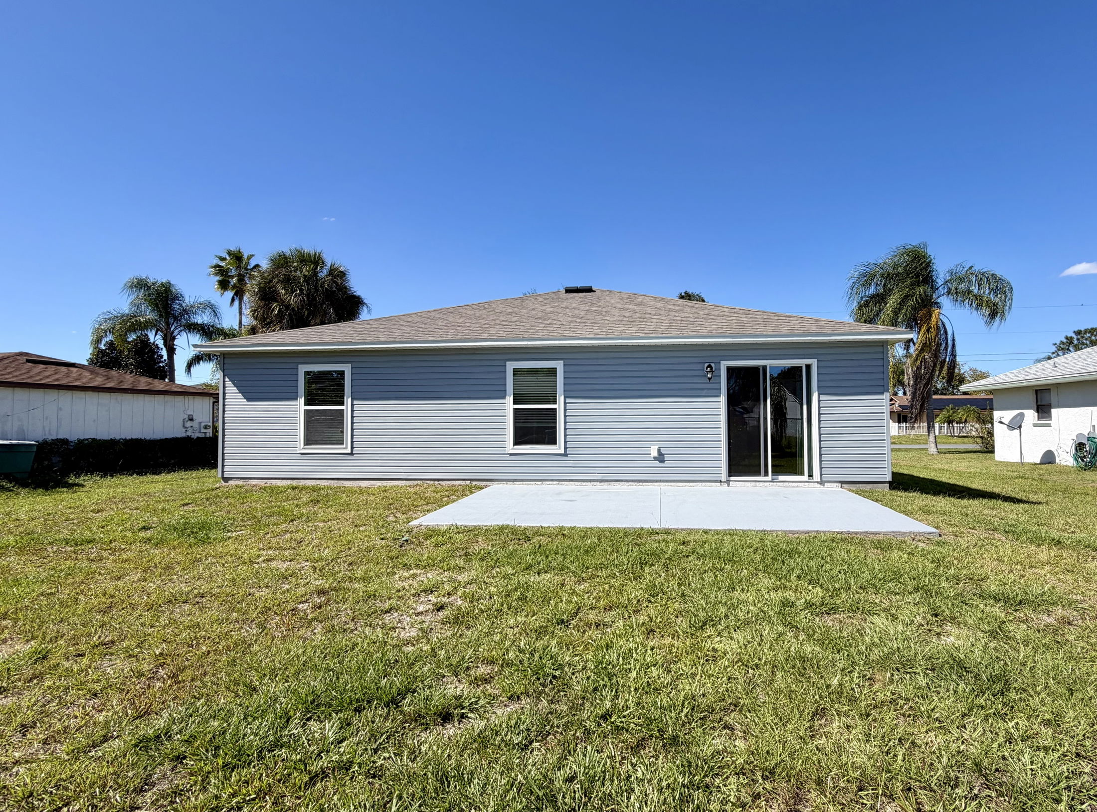 Rear view of a gray single-story house with a patio and lawn under a clear blue sky.