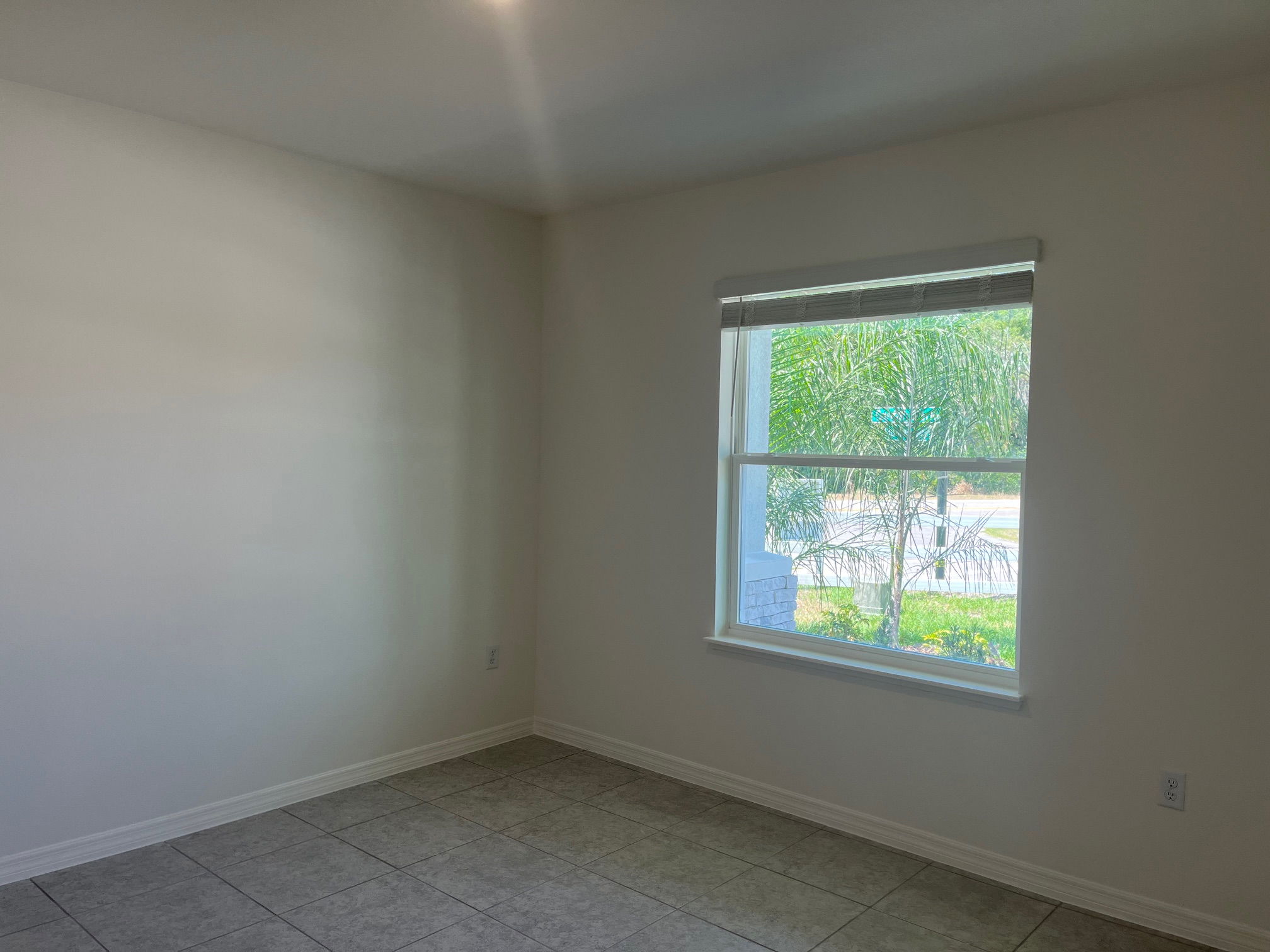 Empty room with tiled flooring and a large window showcasing a view of greenery outside.