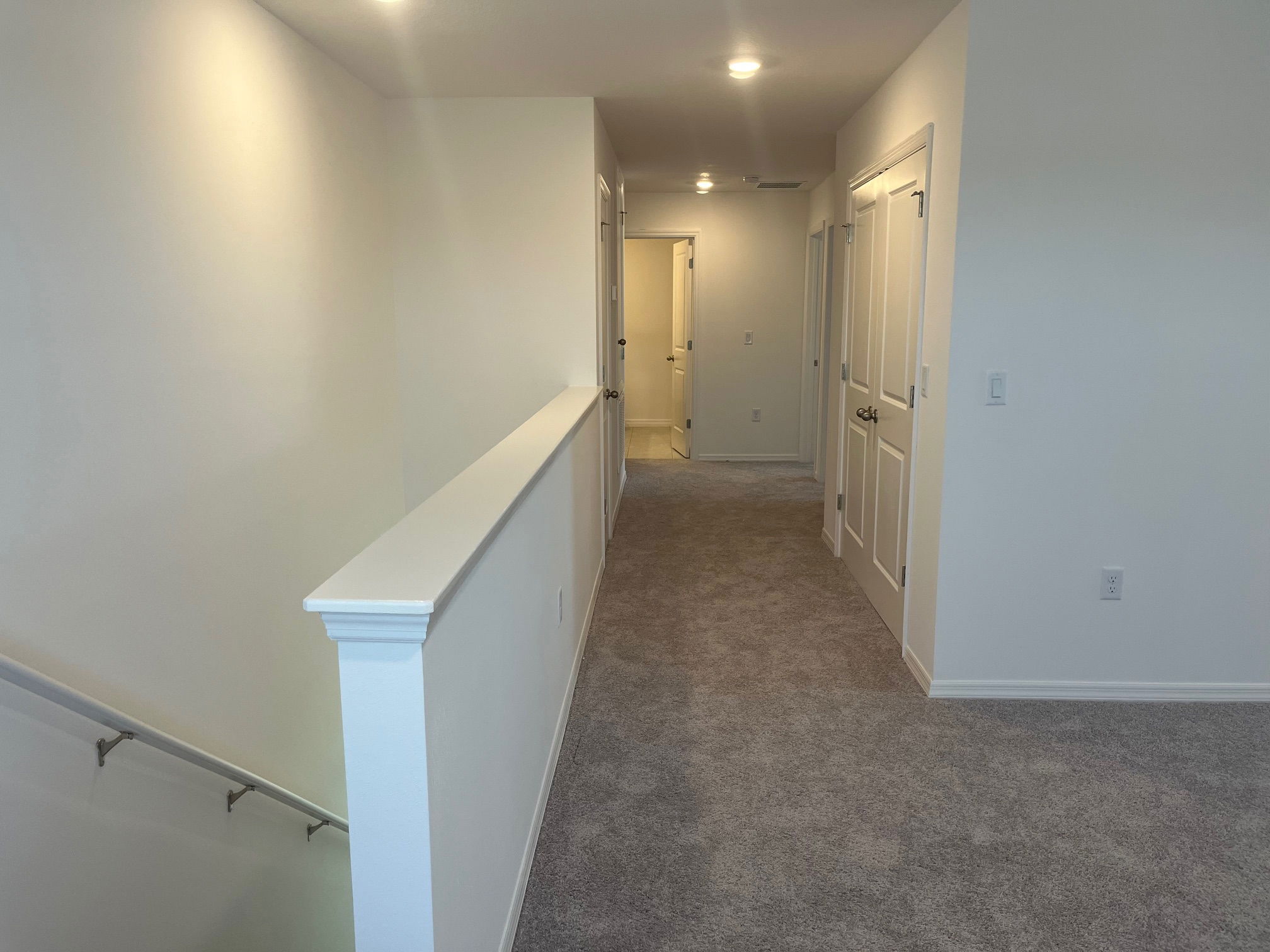 Contemporary upstairs hallway with carpet flooring and multiple doors in a well-lit modern home.