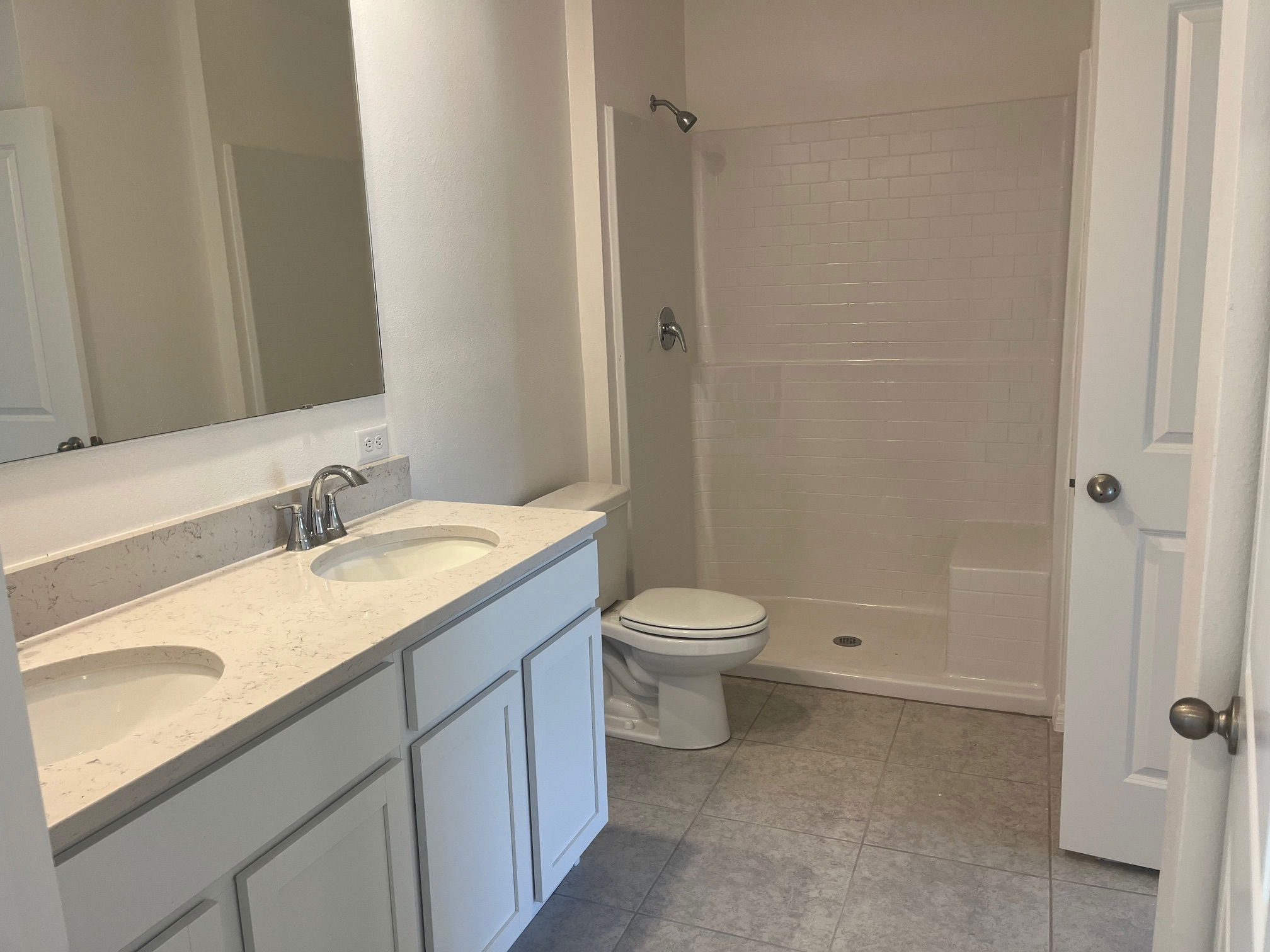 Modern bathroom with a white double sink vanity, spacious walk-in shower, and tiled flooring.