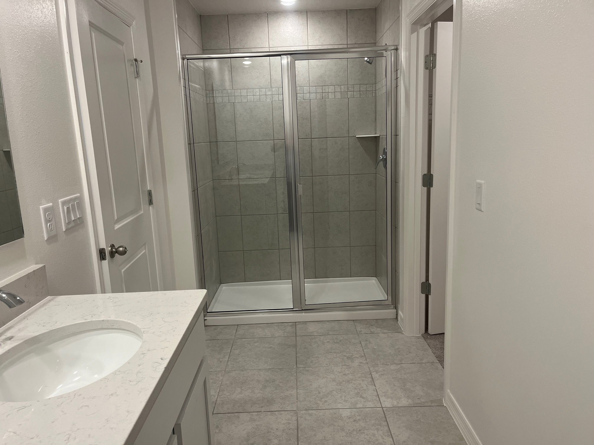 Modern bathroom with a glass-enclosed shower, tiled walls, and a white countertop sink.