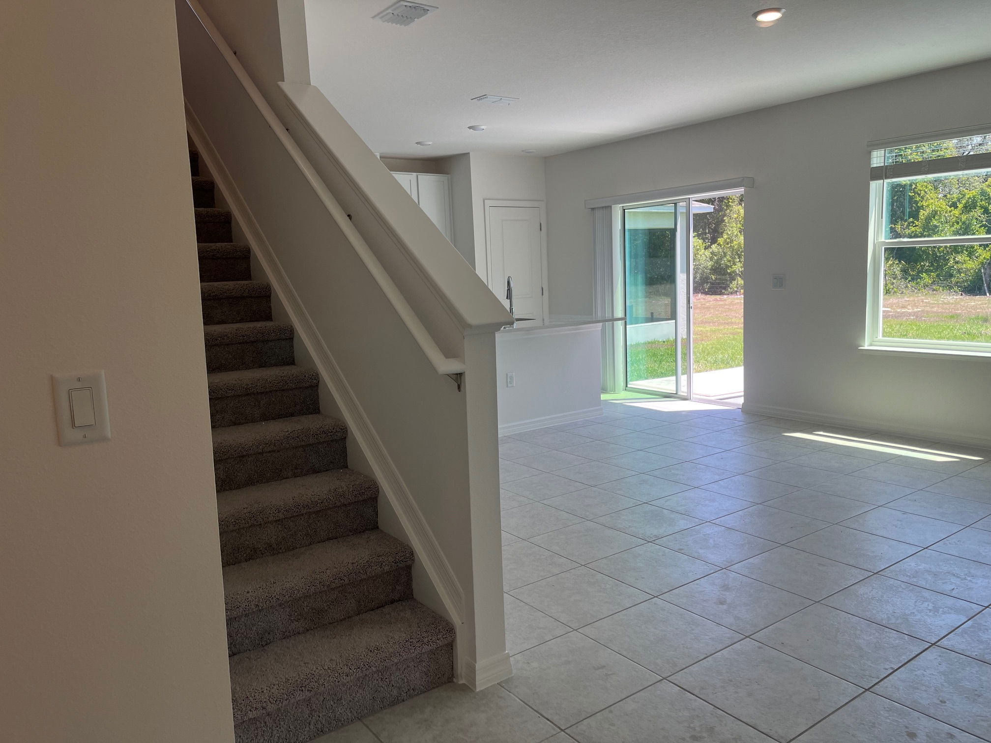 Bright, modern interior with tiled flooring, carpeted stairs, and sliding glass doors opening to a patio with a view.