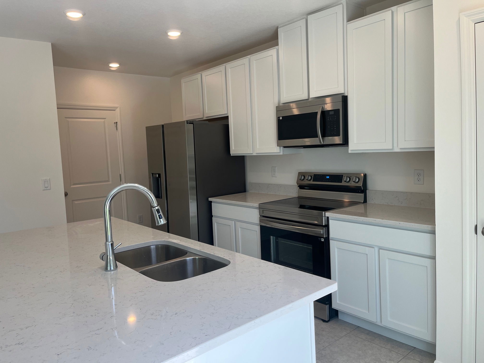 Modern kitchen with white cabinets, stainless steel appliances, and an island featuring a double sink and marble countertop.