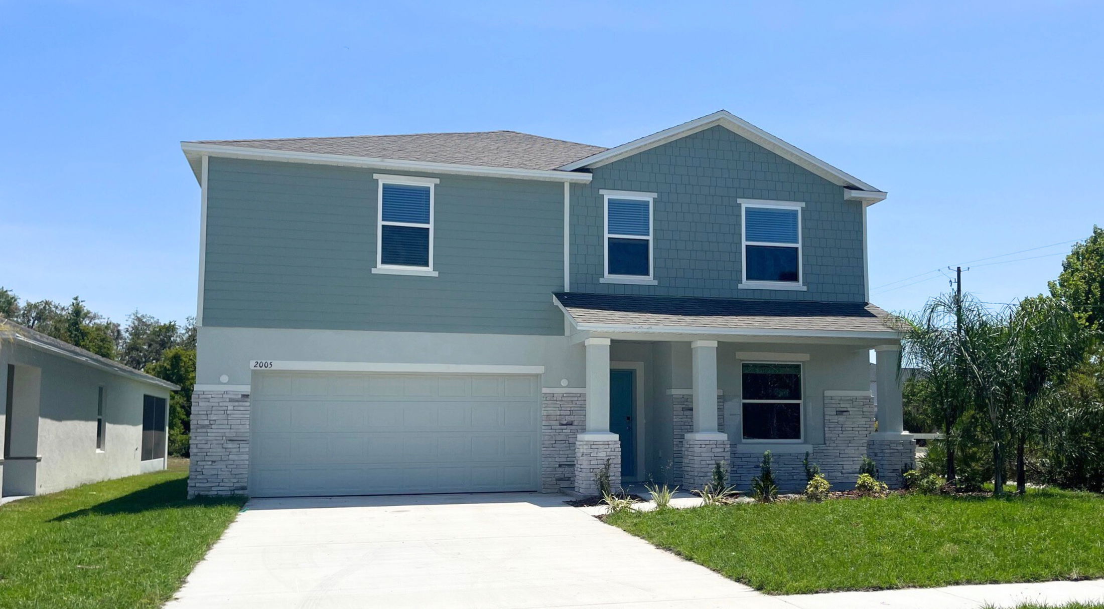 Two-story modern suburban home with a gray exterior, attached garage, and green lawn, under a clear blue sky.
