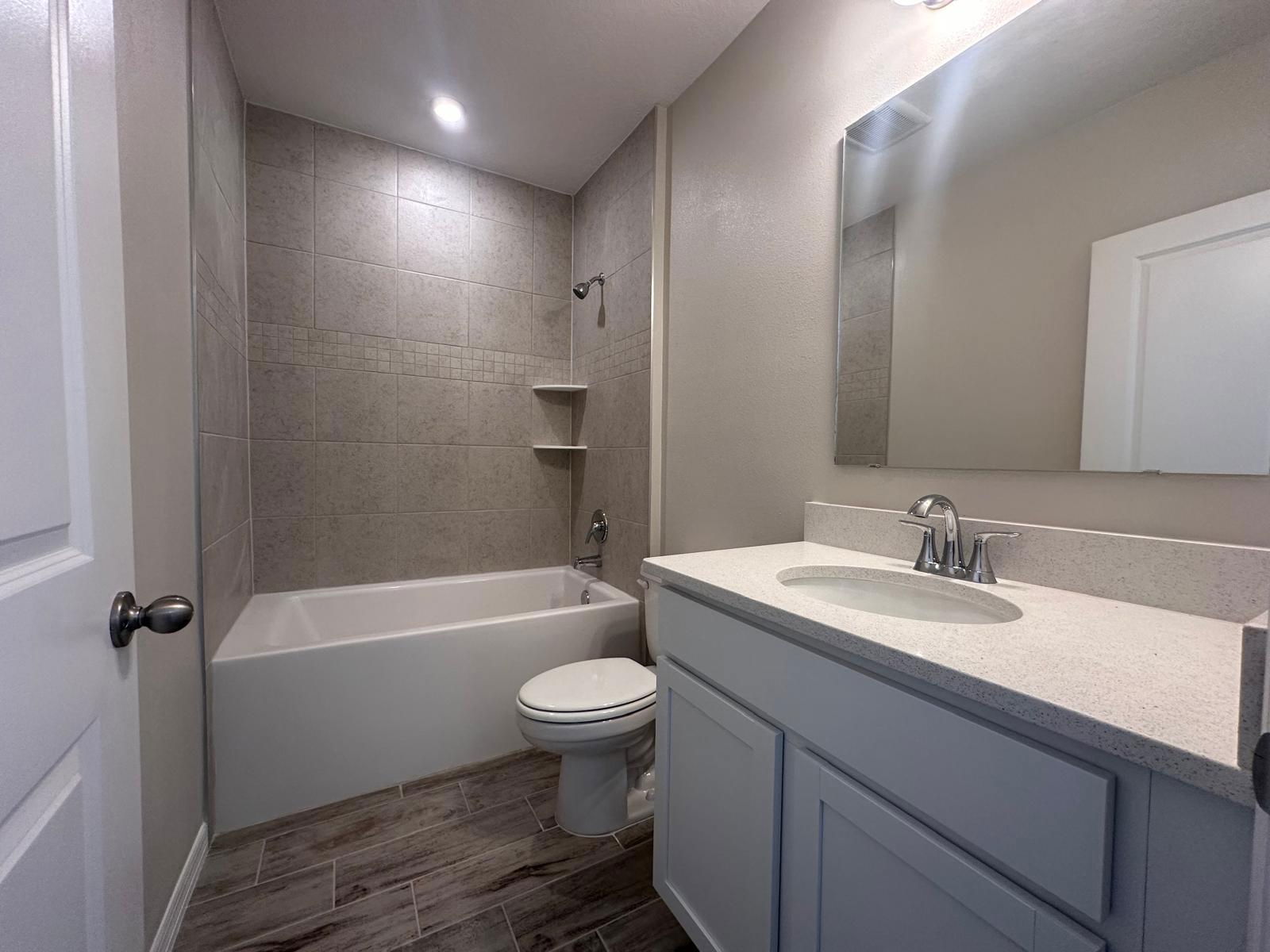 Modern bathroom with sleek white fixtures, granite countertop, and tiled shower walls.