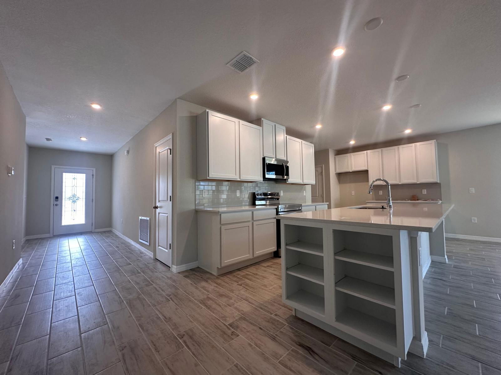 Modern kitchen interior with sleek white cabinetry, stainless steel appliances, and a spacious island under recessed lighting.