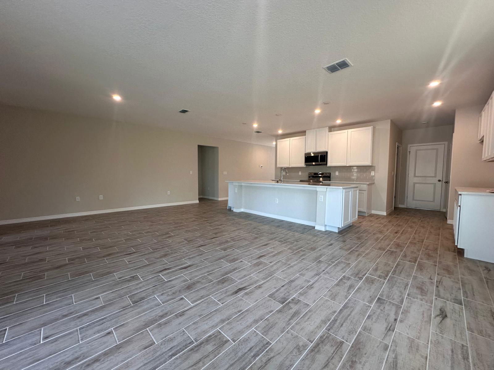 Spacious open-concept modern kitchen and living area with wood-look tile flooring and white cabinetry.