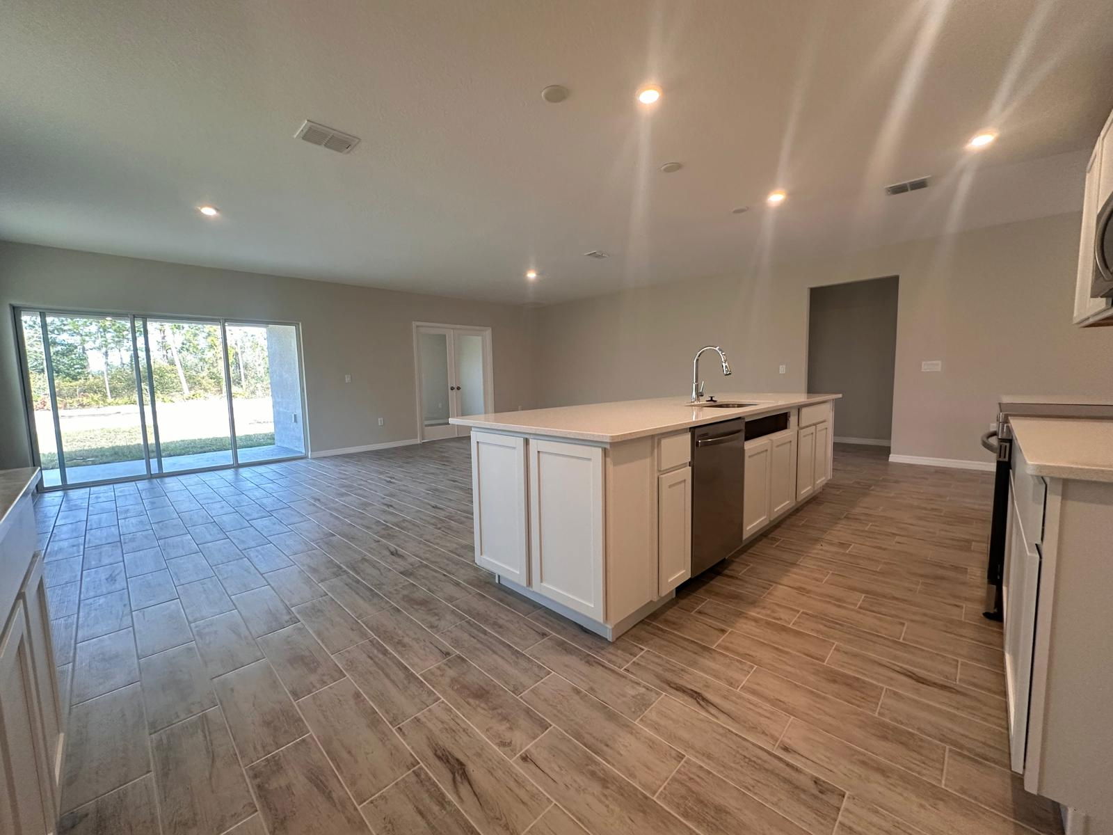 Modern open-concept kitchen and living room with tile flooring, large island, and sliding glass doors leading to a backyard.