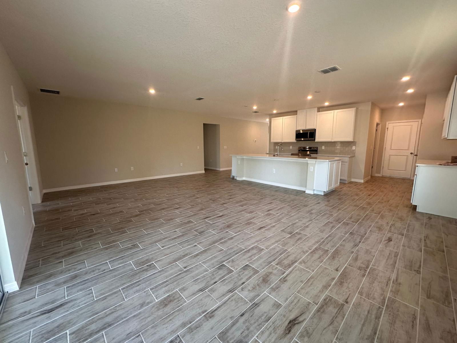 Spacious open-concept living area and modern kitchen with wooden tile flooring in a newly built home.