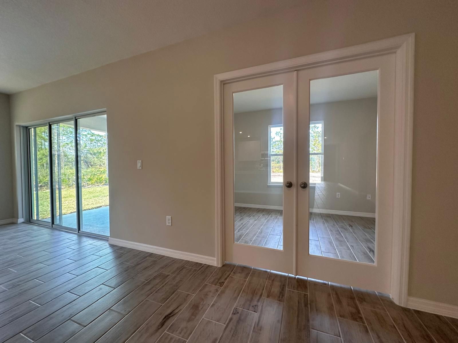 Modern interior room with glass patio doors, wood-look tile flooring, and a view of the outdoor landscape.