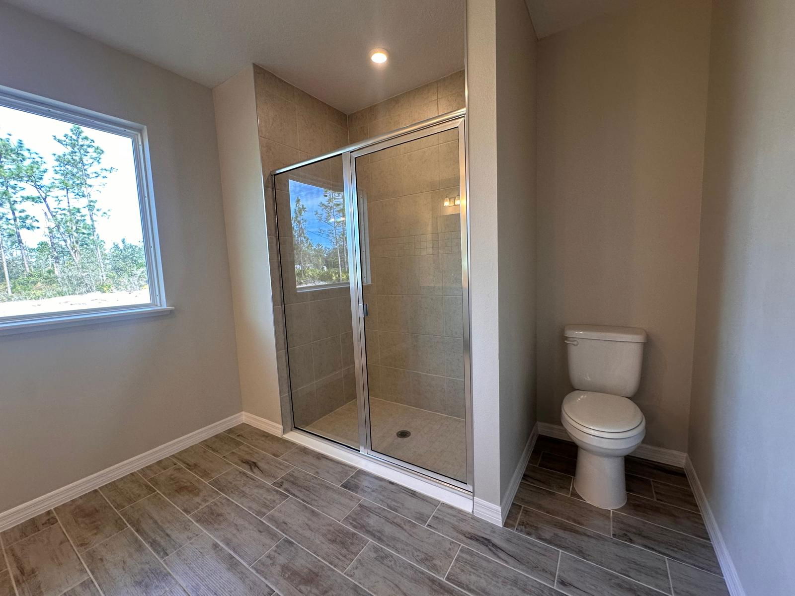 Modern bathroom featuring a glass-enclosed shower, beige tiles, and a white toilet on wood-style flooring.