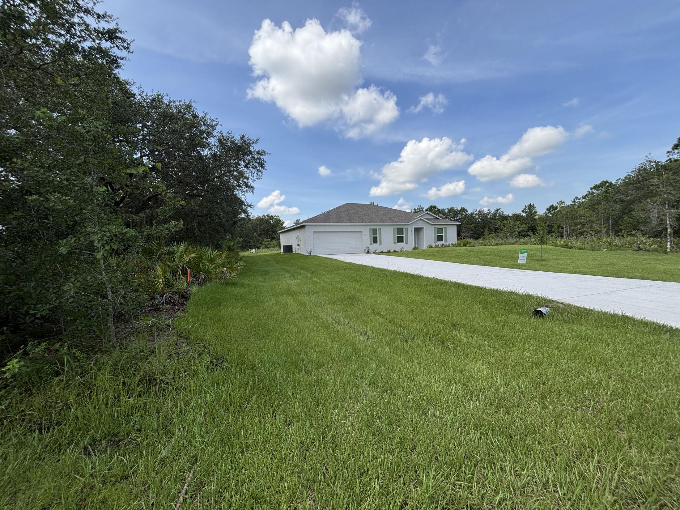 Single-story white house with attached garage, large green lawn, and long driveway under a partly cloudy sky.