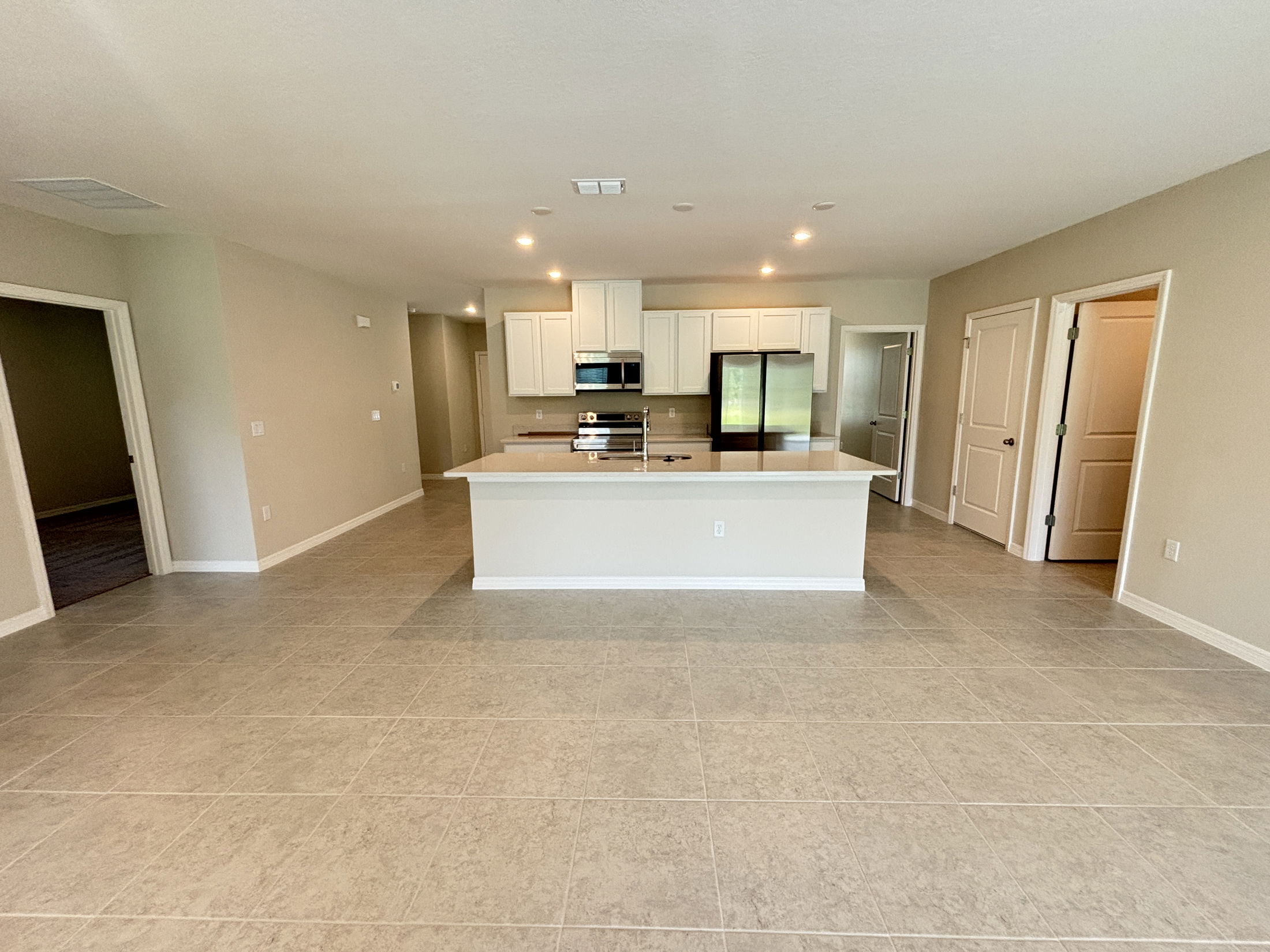 Modern open-concept kitchen with white cabinetry, center island, stainless steel appliances, and tiled flooring.