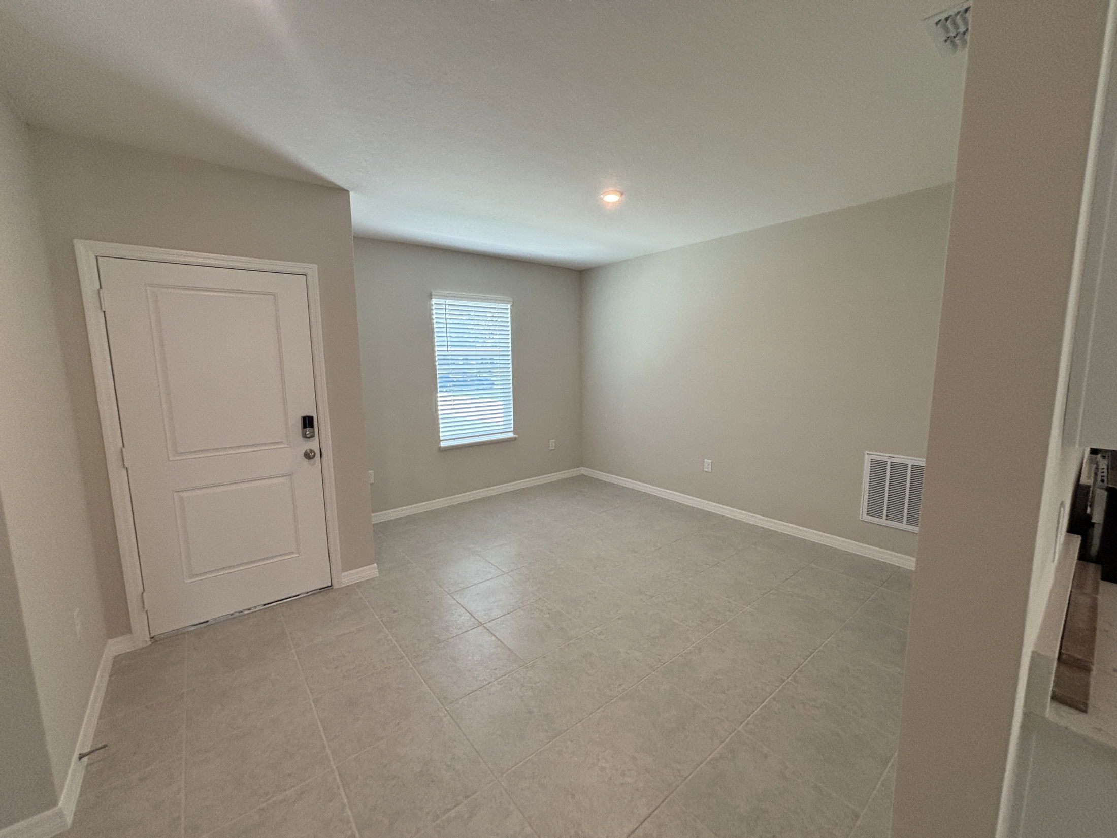 Empty room with beige walls, tiled floor, white door, and window with blinds in a minimalist home interior.