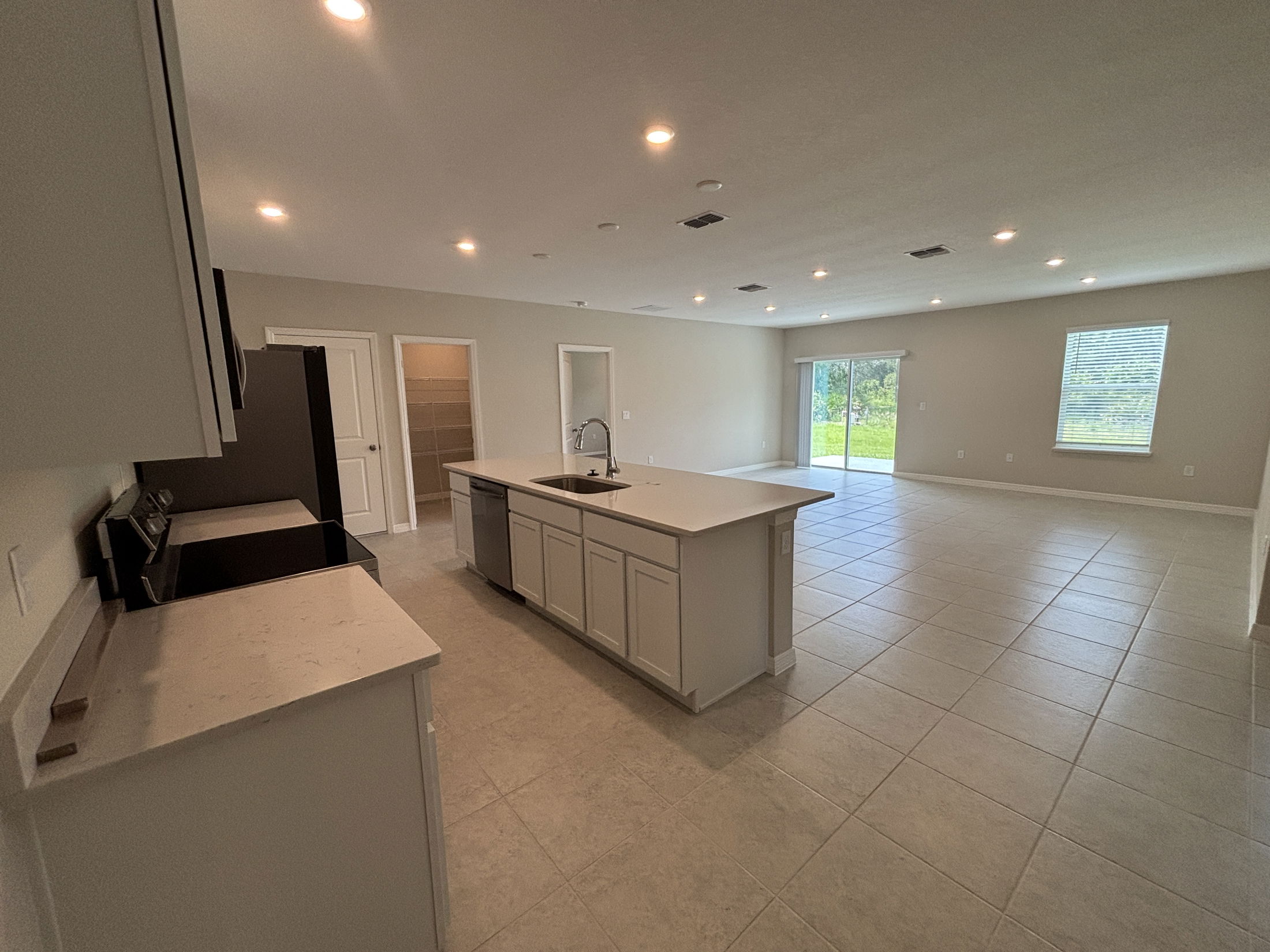 Spacious open-plan kitchen and living area with modern lighting, large windows, and sliding glass doors for natural light.