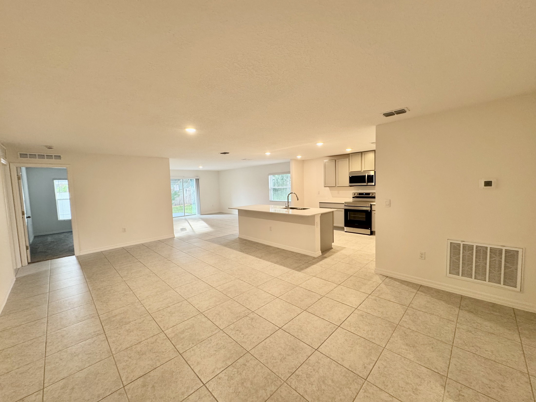 Spacious, open-concept living area featuring tile flooring, a kitchen island, and large windows allowing natural light.