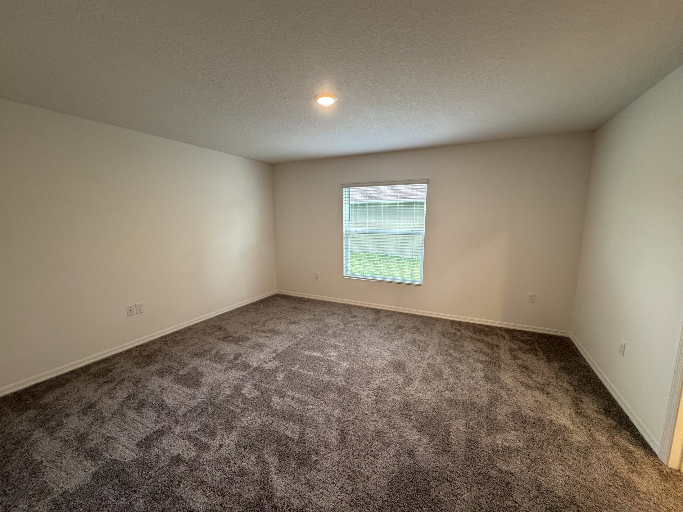 Empty room with light gray carpet, white walls, and a window letting in natural light.