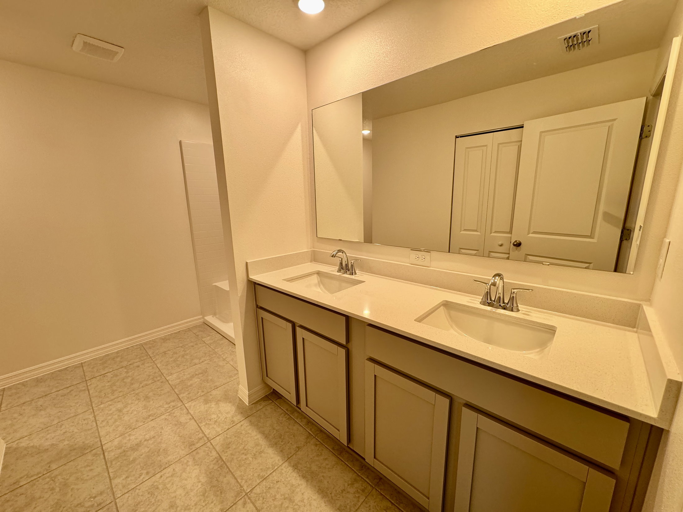 A bathroom with dual sinks, a large mirror, and light-colored tile flooring.