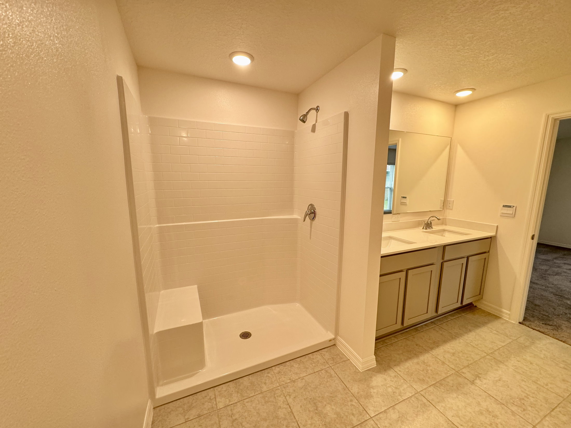 A clean bathroom featuring a walk-in shower, double sink vanity, and tiled floor.