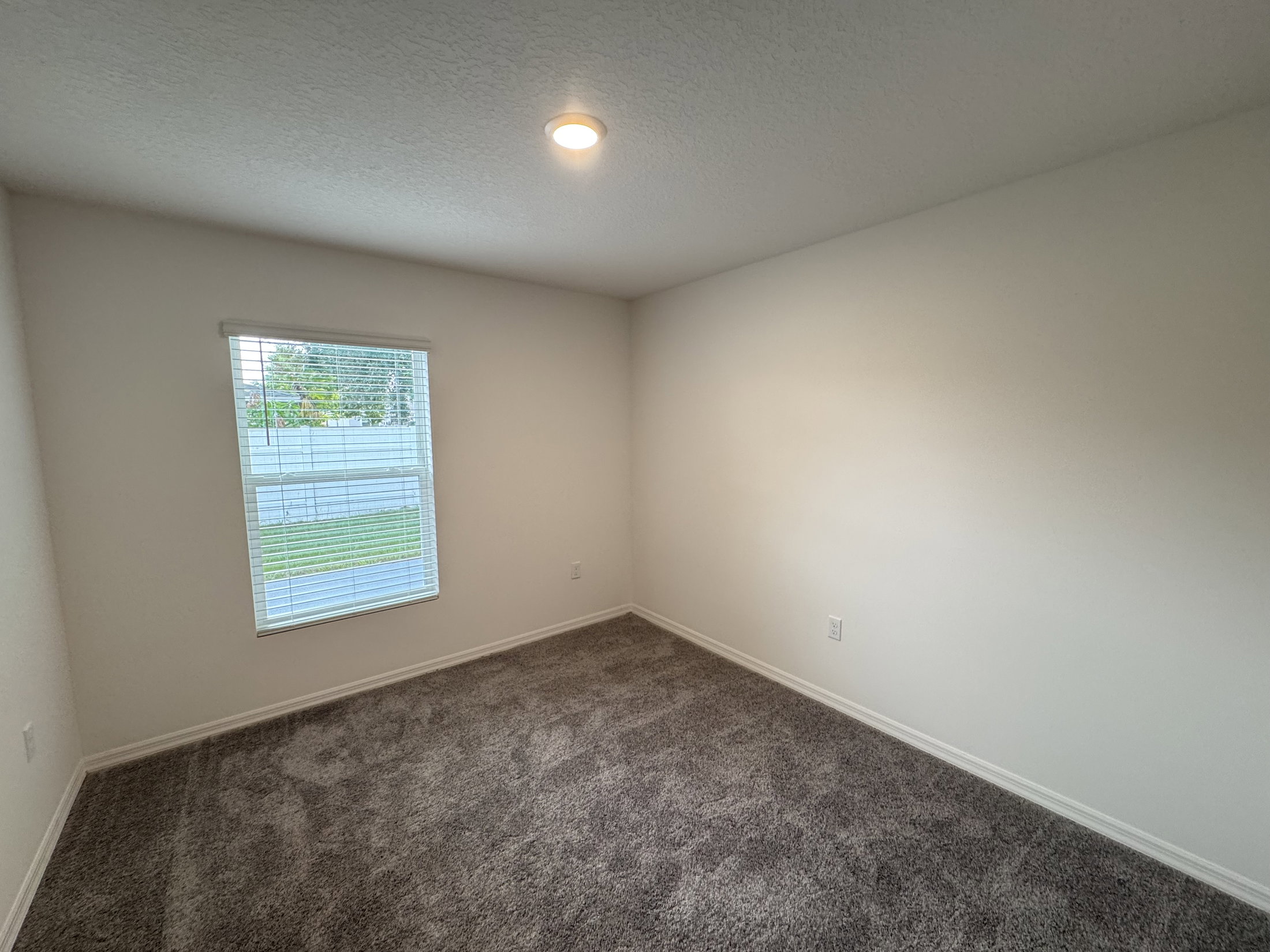 A vacant room with light gray carpet, white walls, and a window letting in natural light.