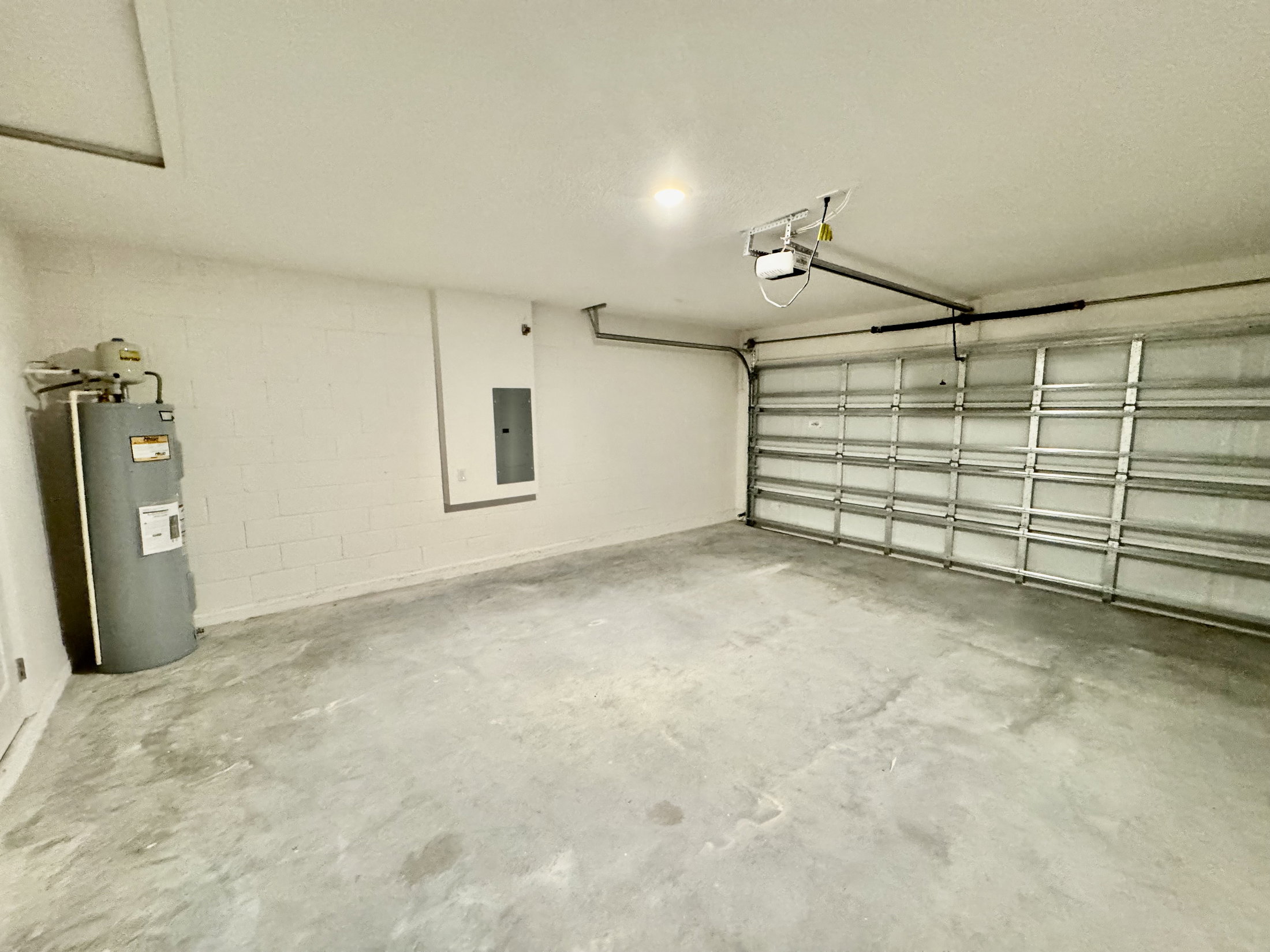 Empty garage with a concrete floor, a closed garage door, and a water heater mounted on the wall.