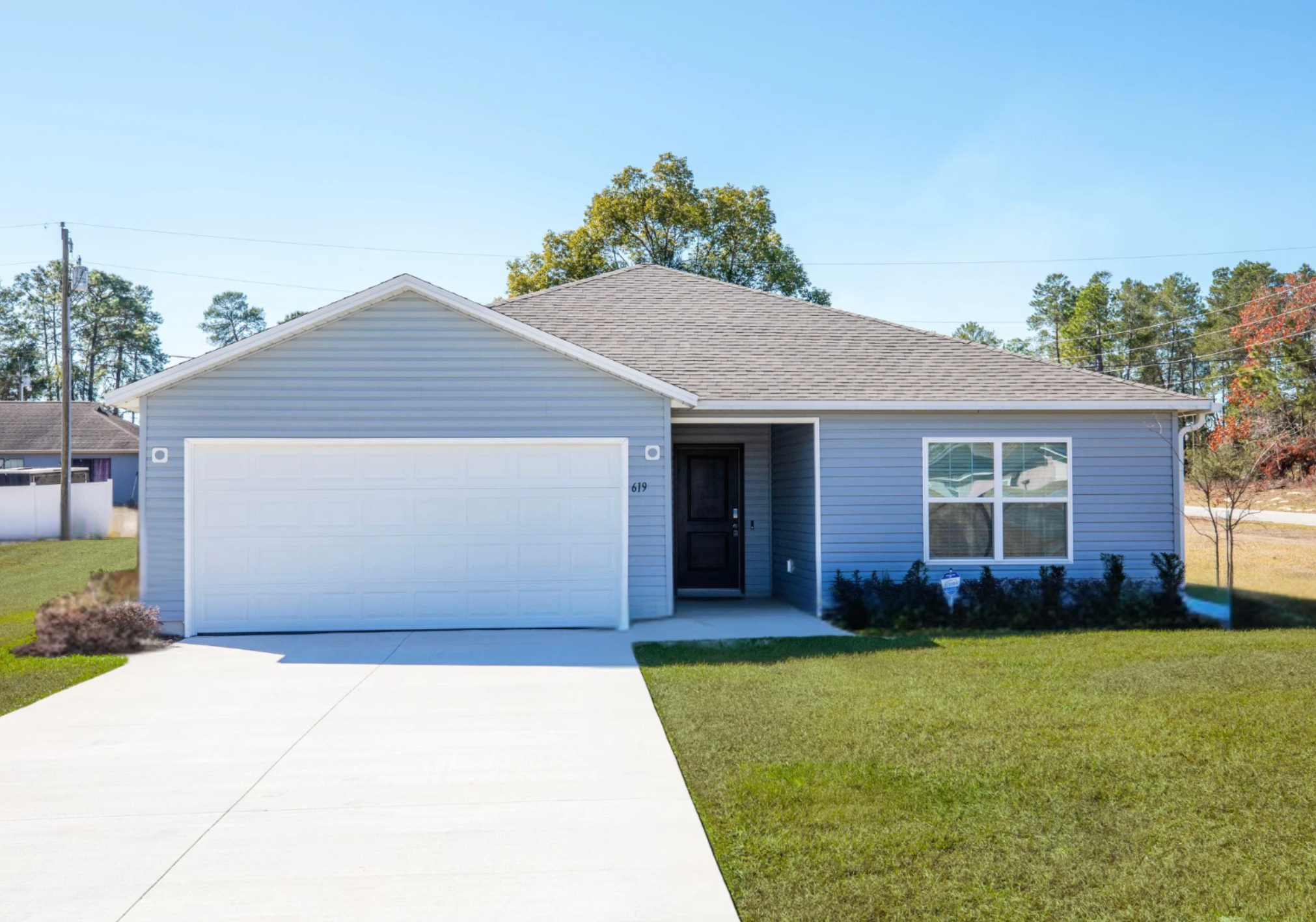 Single-story blue house with a gray roof, a front porch, and a two-car garage, surrounded by a green lawn.
