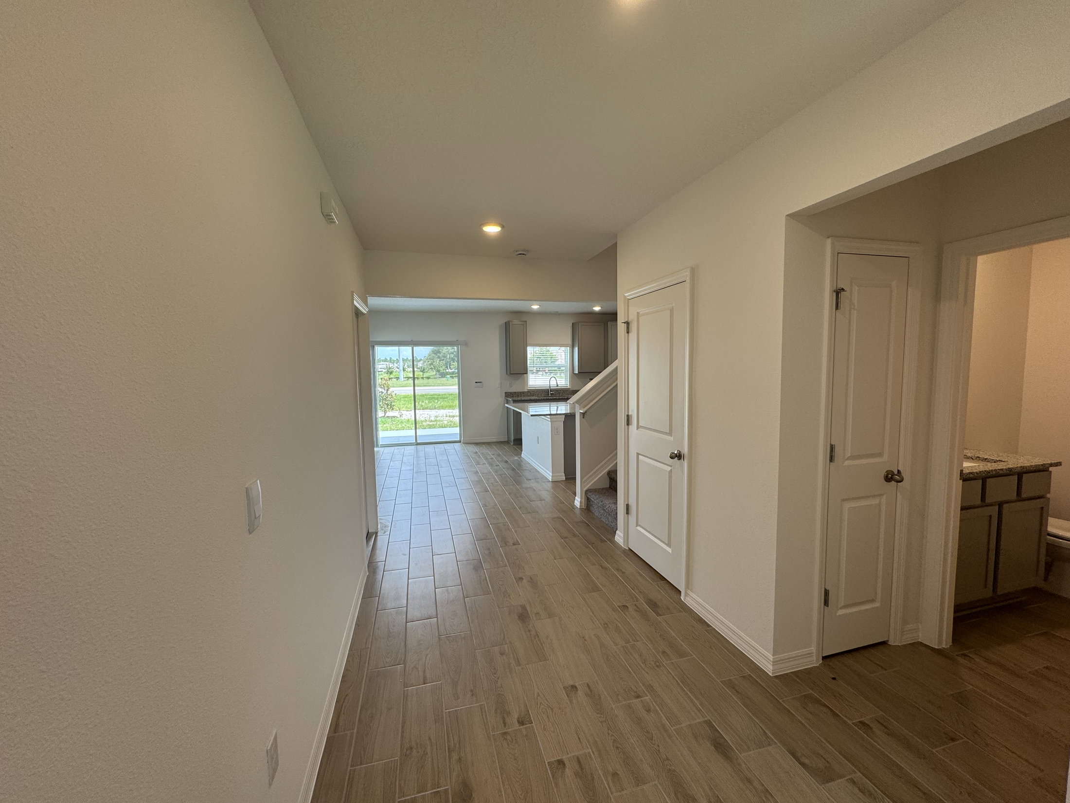 Interior view of a modern home showing a hallway leading to a kitchen and living area with large windows.
